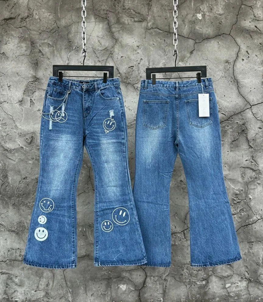 Two pairs of blue jeans hanging on black hangers against a cracked gray concrete wall, with white smiley face and doodle stickers on the front of the jeans on the left.
