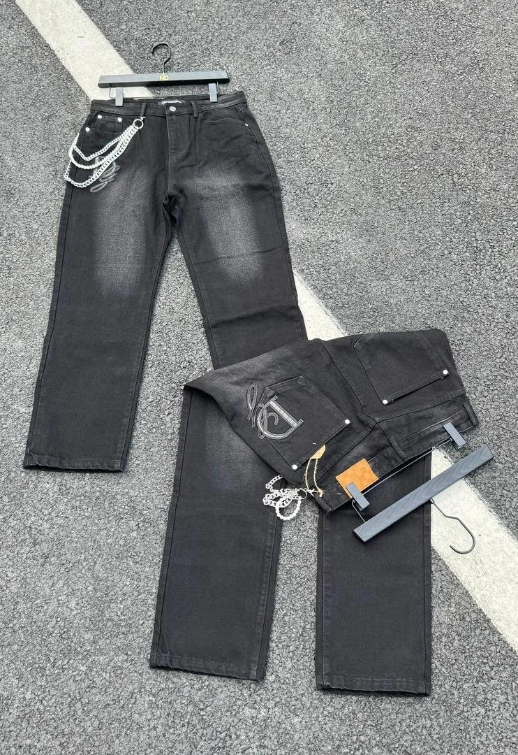 Two pairs of black jeans, one on a hanger and one folded, placed on a gray parking lot with a white line. The jeans on the hanger have a chain attached to the belt loop.