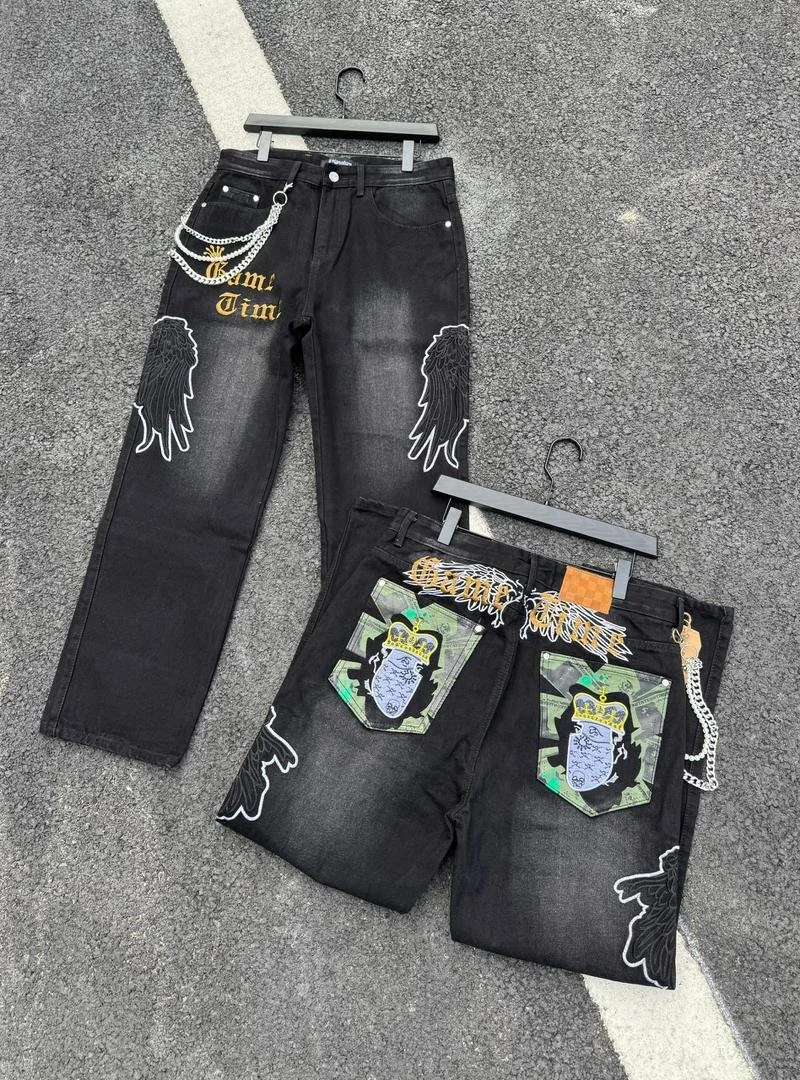 Two pairs of black jeans with graphic patches and embellishments, displayed on hangers on a parking lot surface.