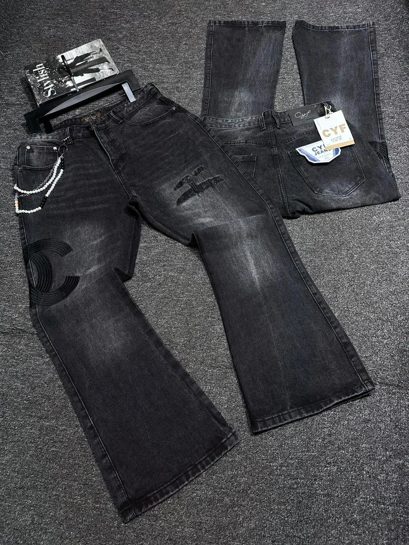 Pair of black jeans with graphic patches, a pair of faded black jeans with tags, and a magazine on a gray carpet.