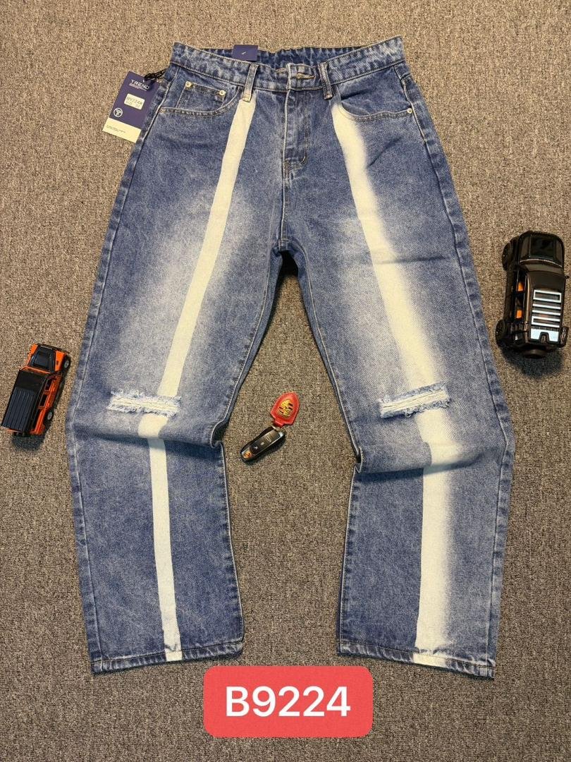 Pair of distressed jeans with white vertical stripes, laid flat on a carpeted surface, accompanied by toy trucks and a key fob, with a red label reading B9224.