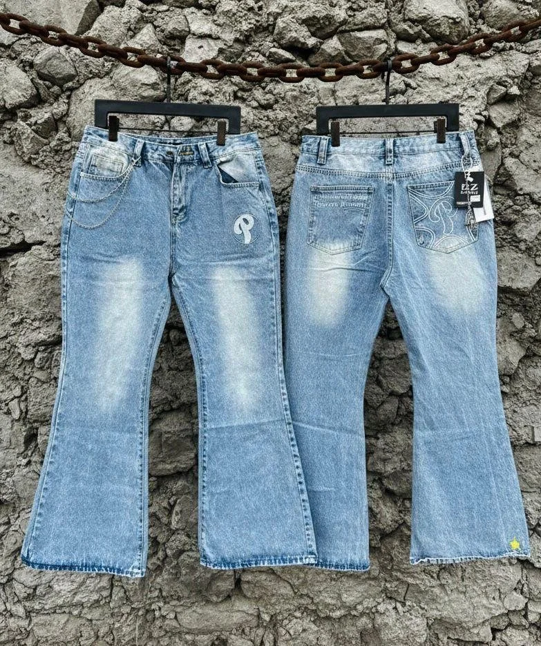 Two pairs of light blue jeans hanging from a chain against a rocky background.
