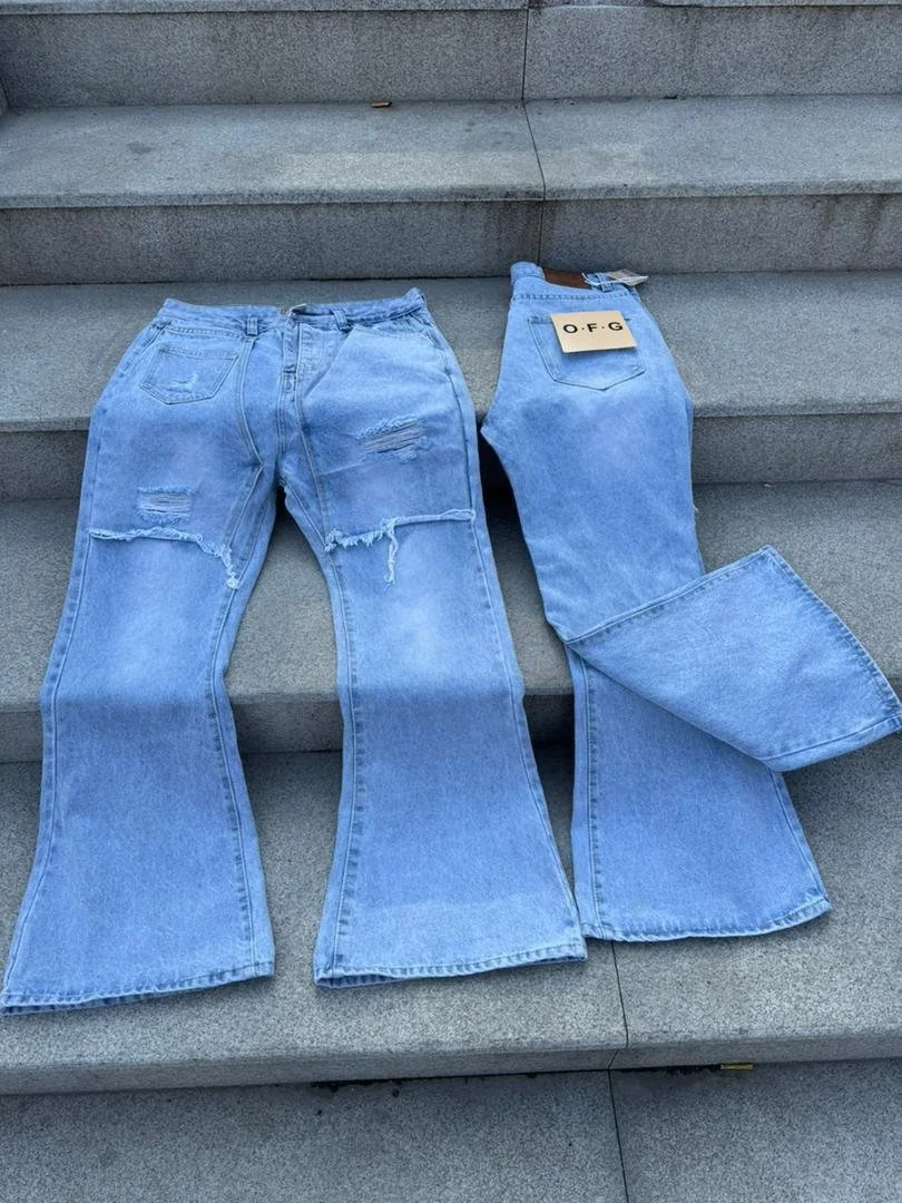 Two pairs of light blue ripped jeans laid out on concrete stairs. The pair on the left has rips on the thighs, the pair on the right has a tag reading 'O.F.G'.