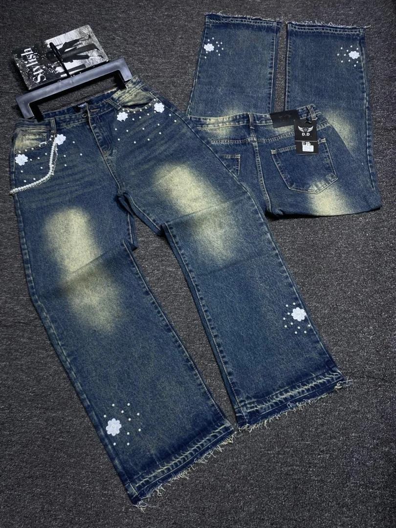 Two pairs of blue jeans with painted white floral and dot designs, laid flat on a dark carpeted surface.