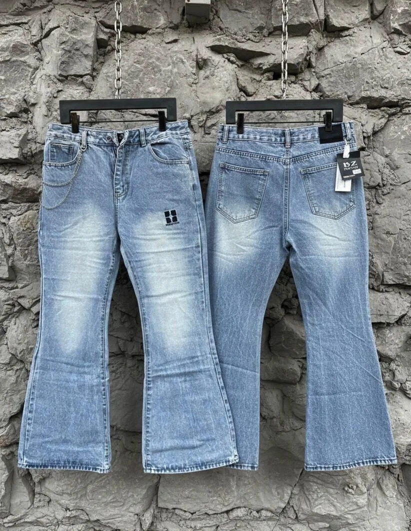 Two pairs of blue jeans hanging on black hangers against a stone wall.
