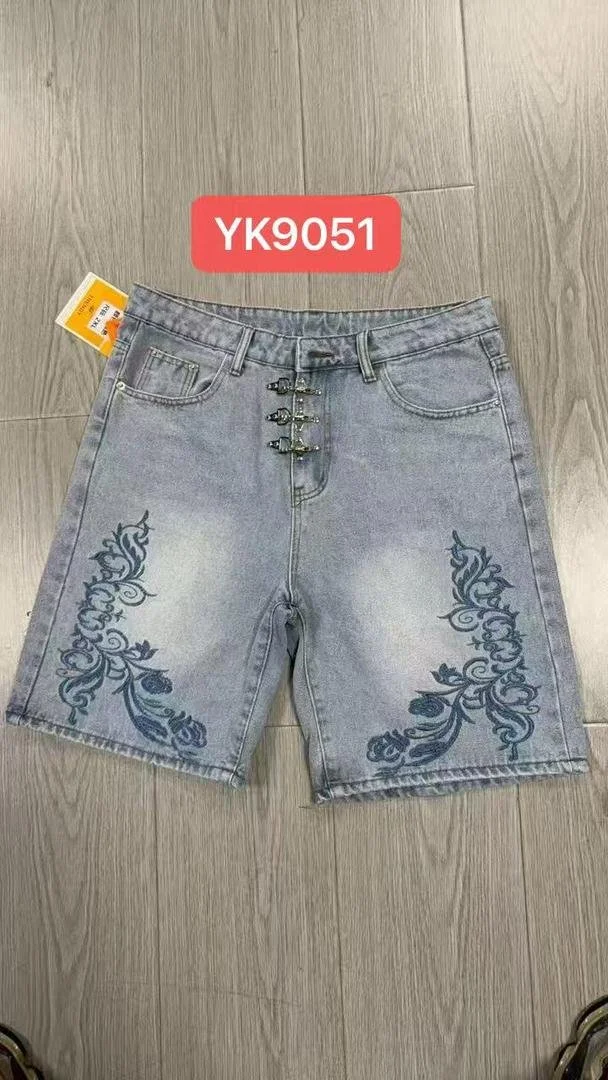 Light blue denim shorts with embroidered dark blue floral designs on the front, displayed on a gray wooden floor.