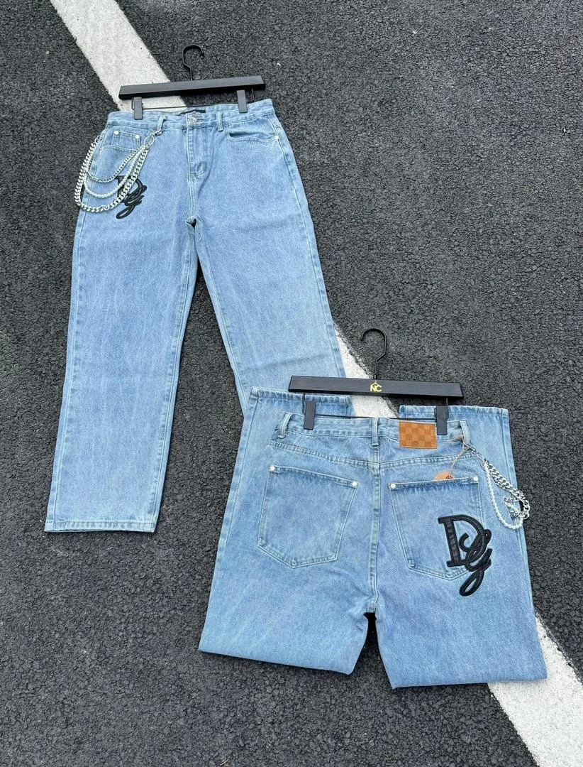 Two pairs of light blue jeans with chain accessories hanging on black hangers, placed on a dark asphalt surface with white painted parking lines.