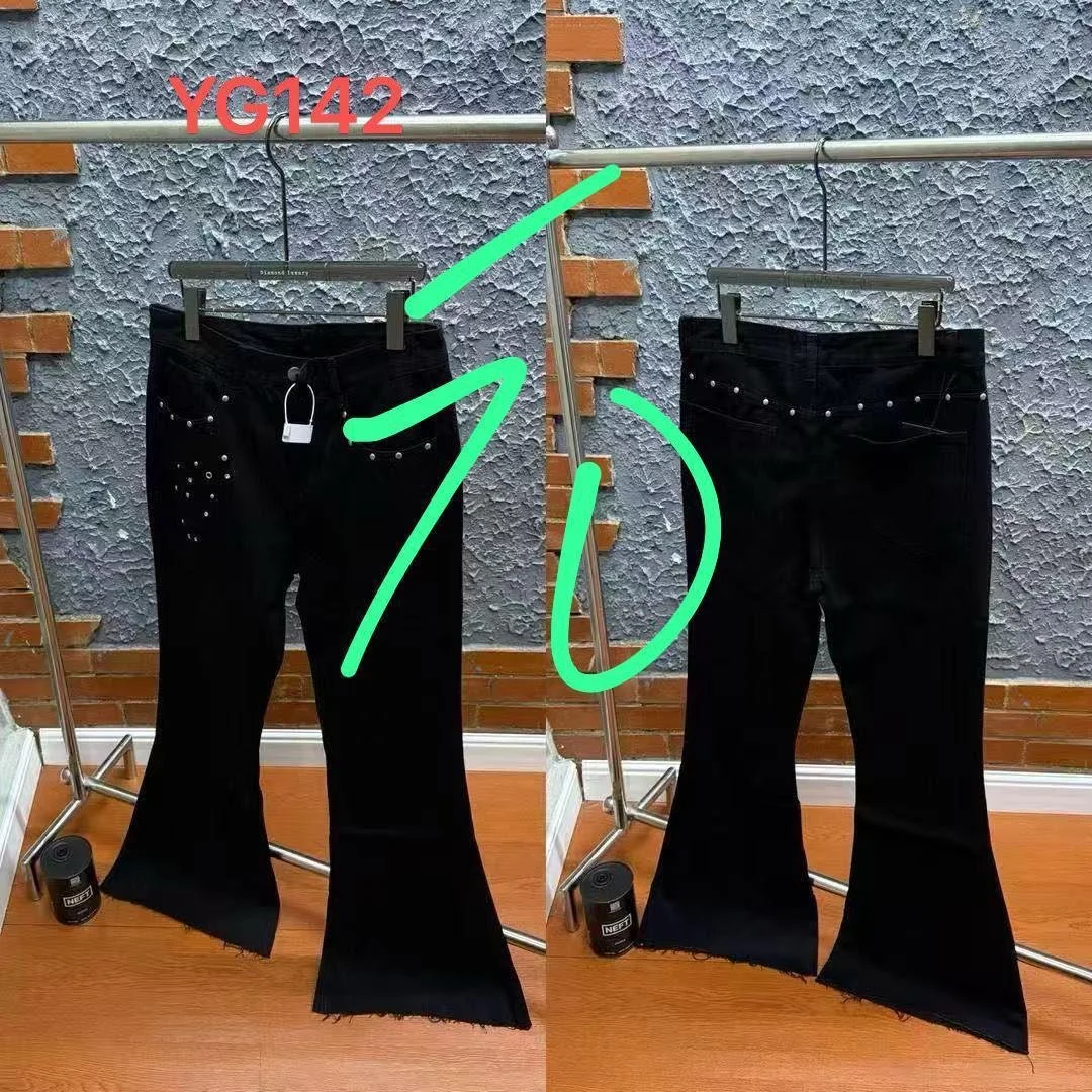 Pair of black jeans with embellishments, displayed on two hangers against a textured wall with brick accents, labeled 'YG142'.