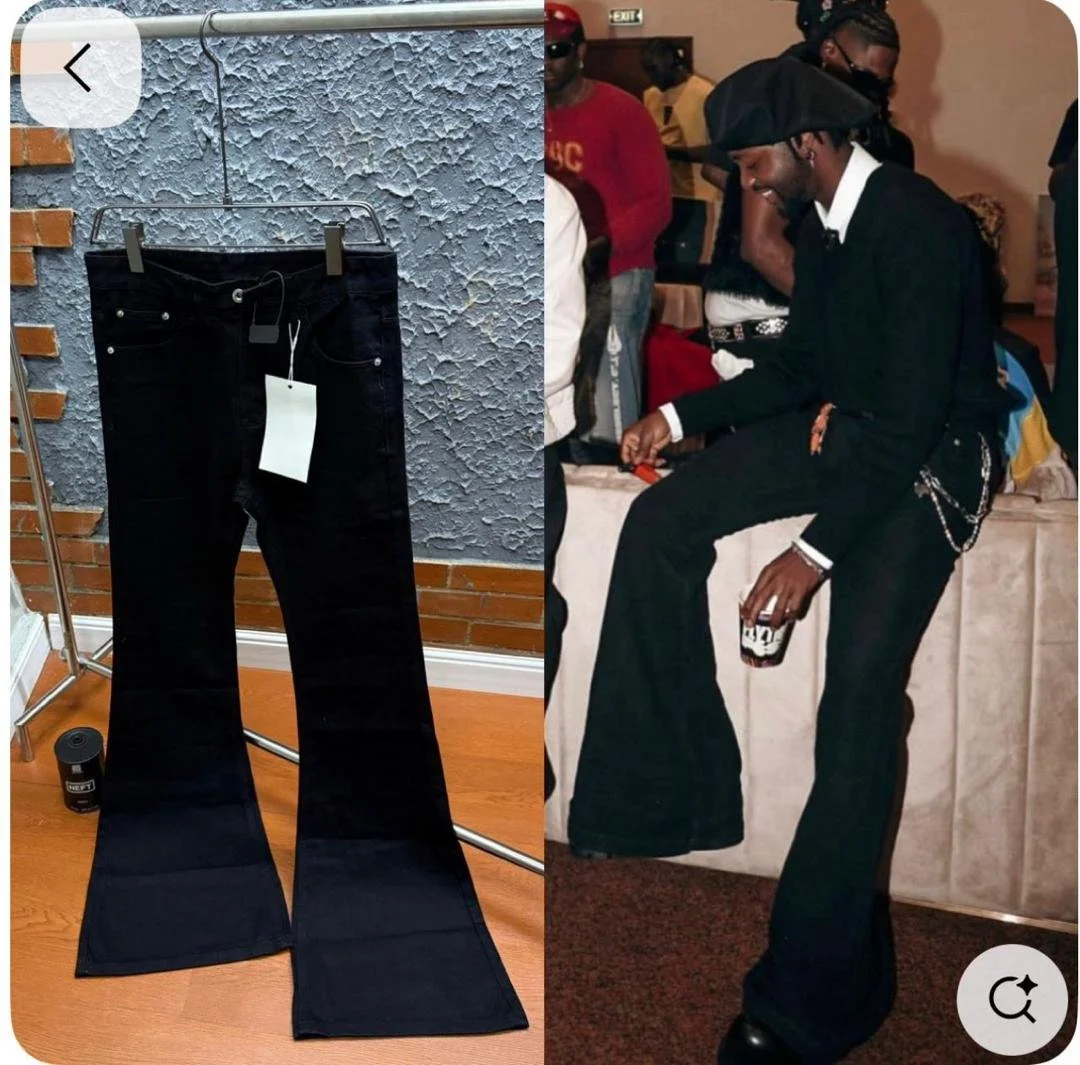 The image shows a pair of black flared jeans hanging on a clothes rack on the left and a man dressed in black pants and a jacket, wearing a black cap, sitting on a bench and holding a drink on the right.