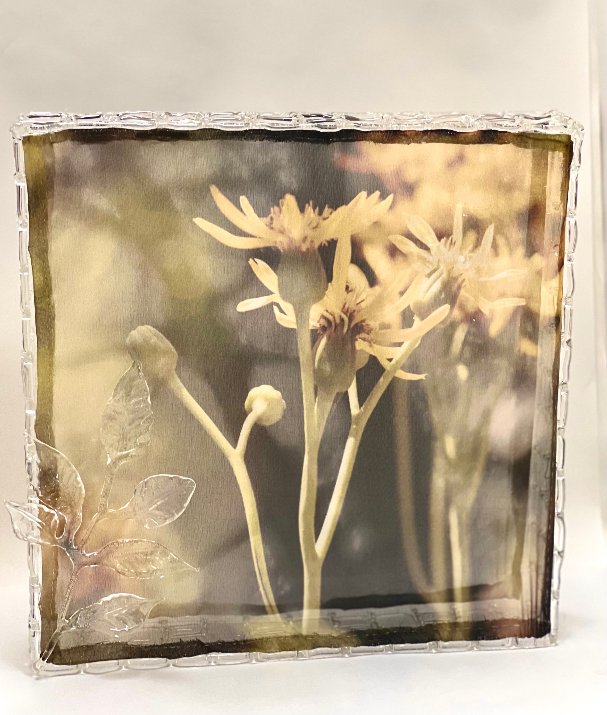 Close-up of a glass block with a floral image inside, featuring cream-colored flowers and leaves, with a textured border.