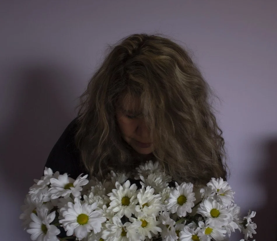 A woman with curly hair looking down at a bouquet of white daisies.