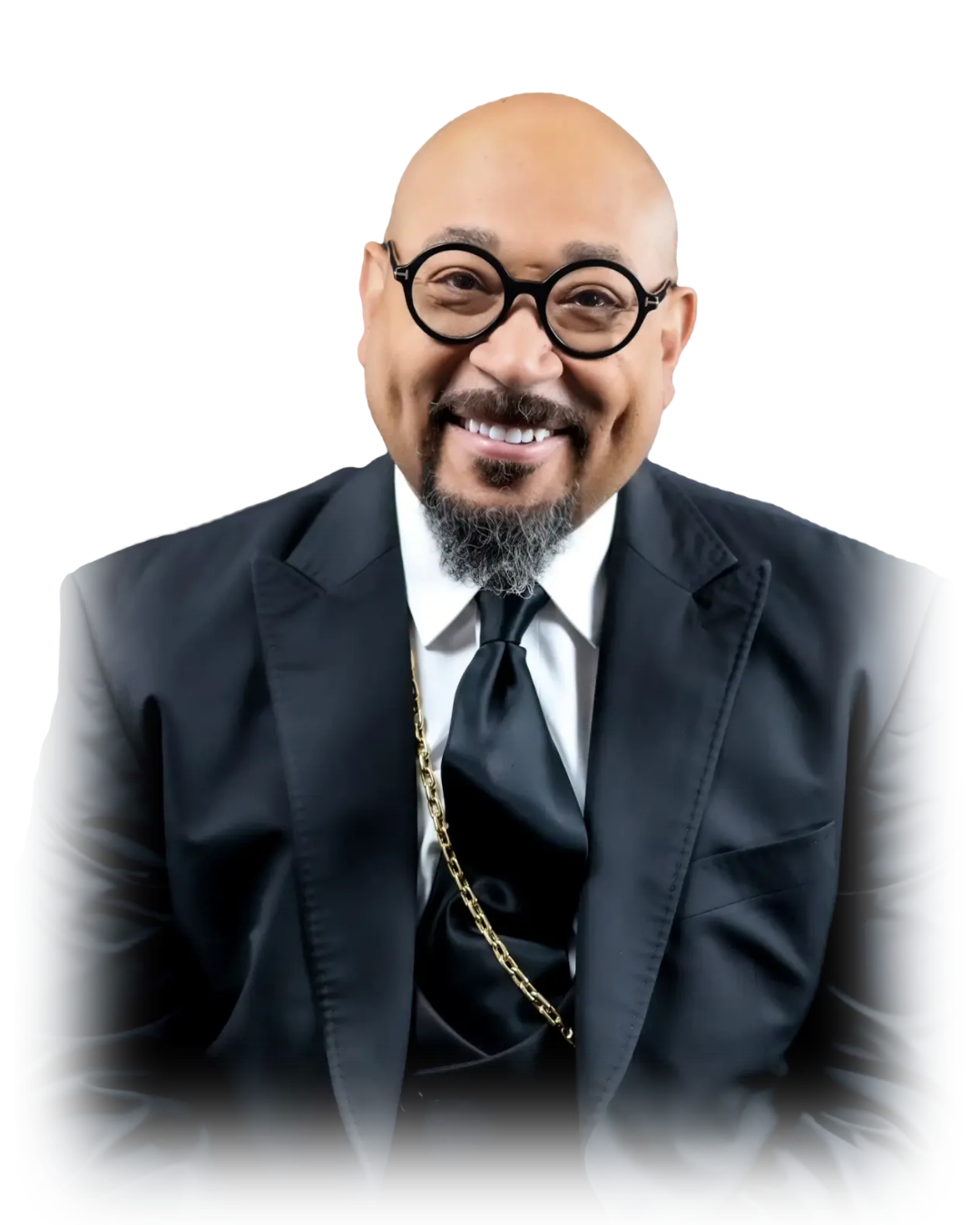 A smiling man in a black suit, white shirt, black tie, round glasses, and a gold chain, against a plain background.