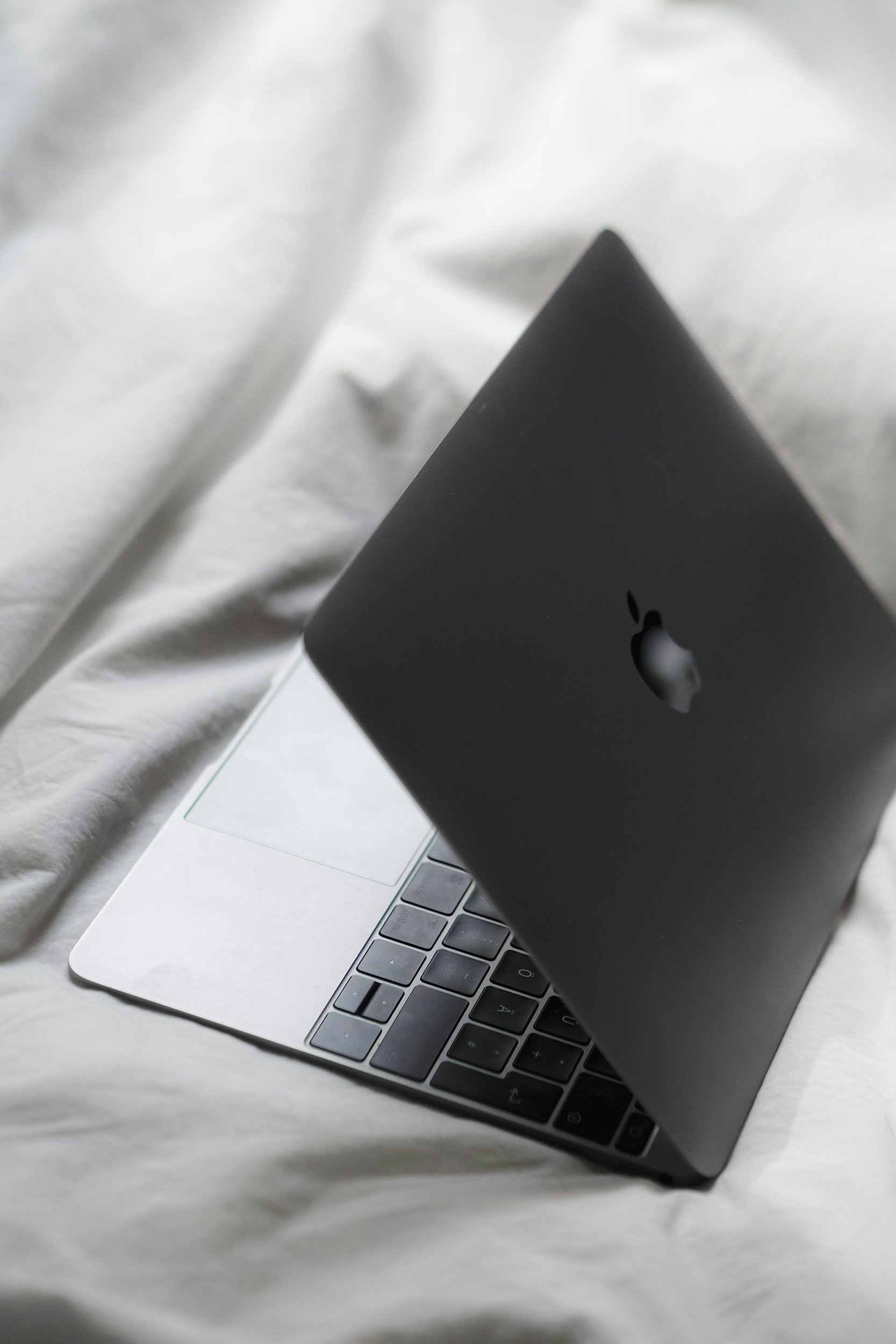 Close-up of a silver MacBook laptop with a black iMac resting on top of it, on a white surface with a soft fabric background.