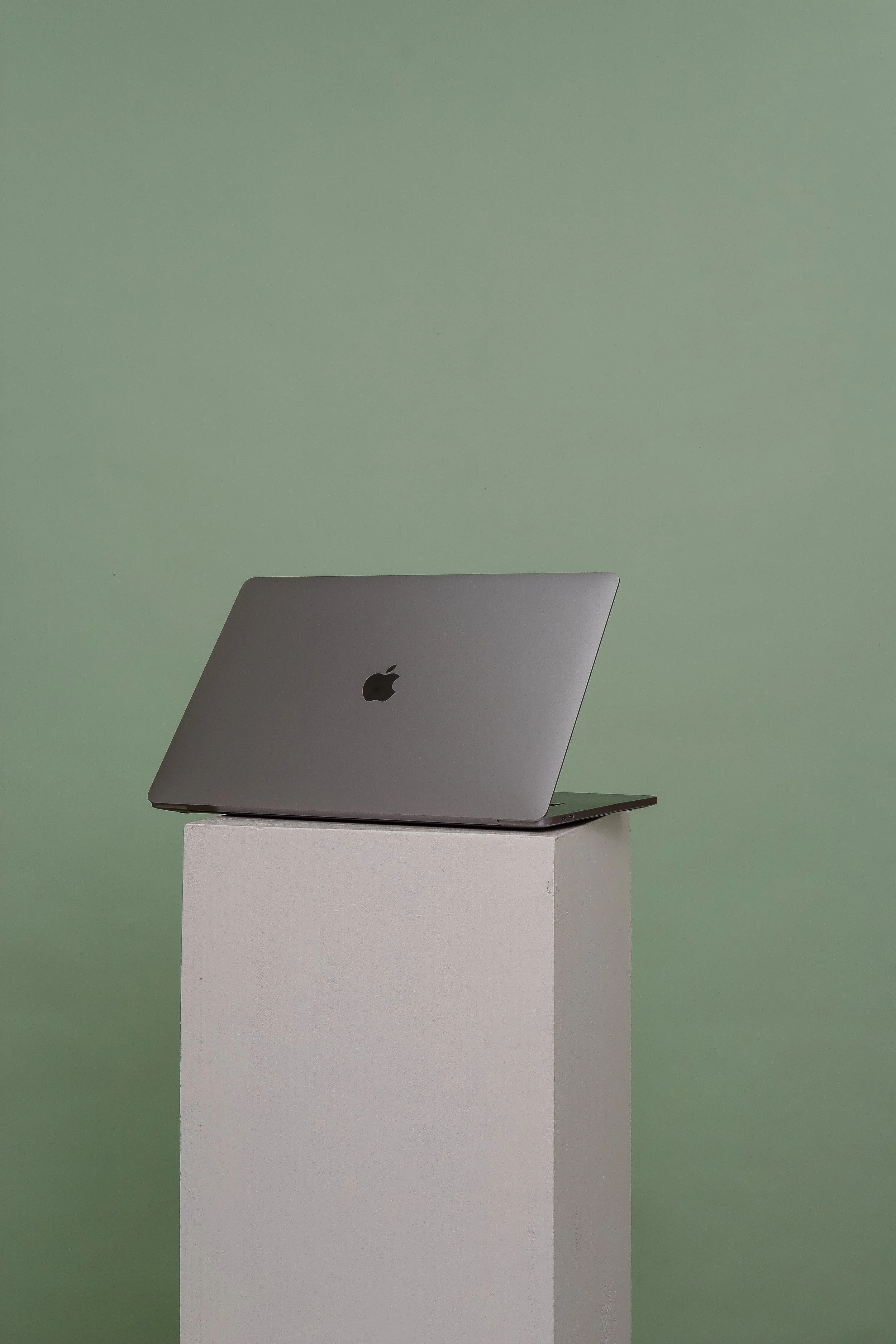 A silver MacBook Pro laptop with the Apple logo on the back of the screen, placed on a white pedestal against a light green background.