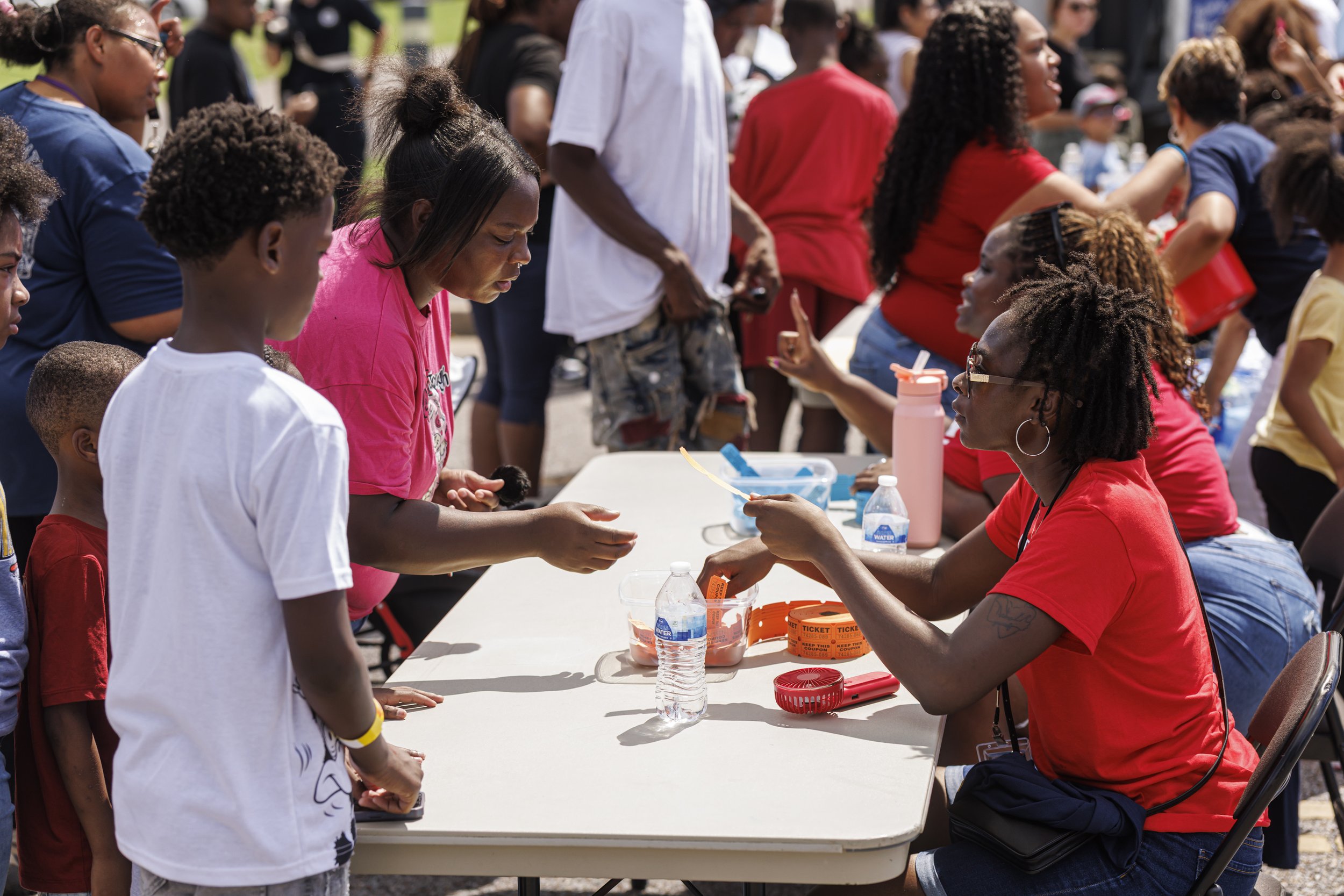 A diverse group of people gathered outdoors around a table, engaging in a community event or fair.