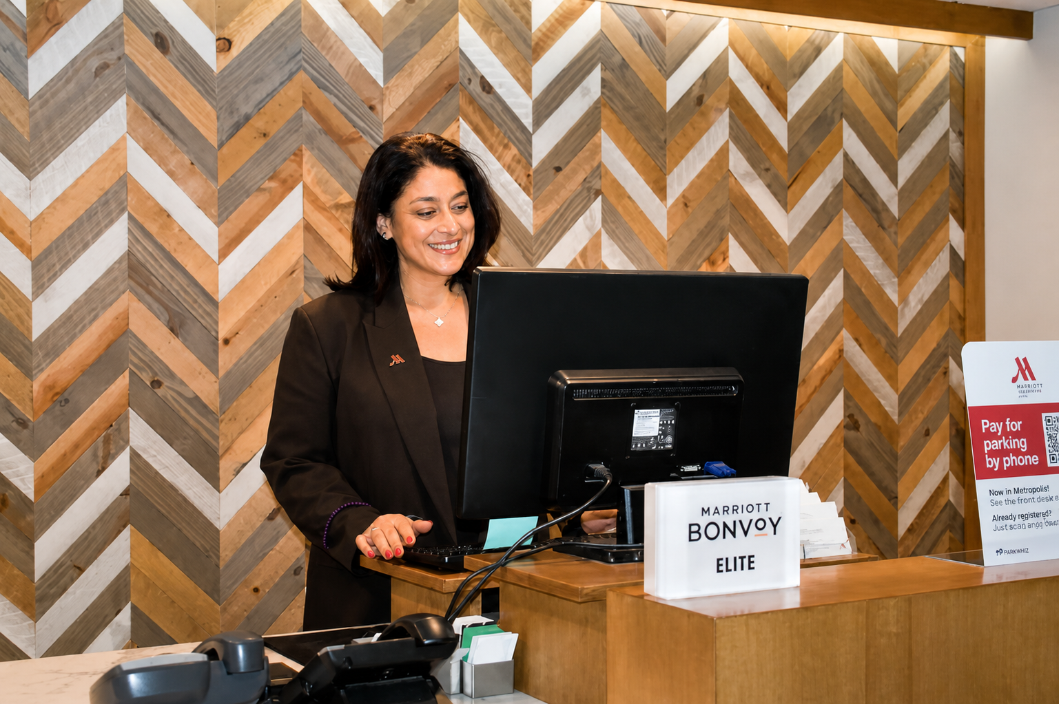 A woman at a hotel check-in counter, smiling at a computer.