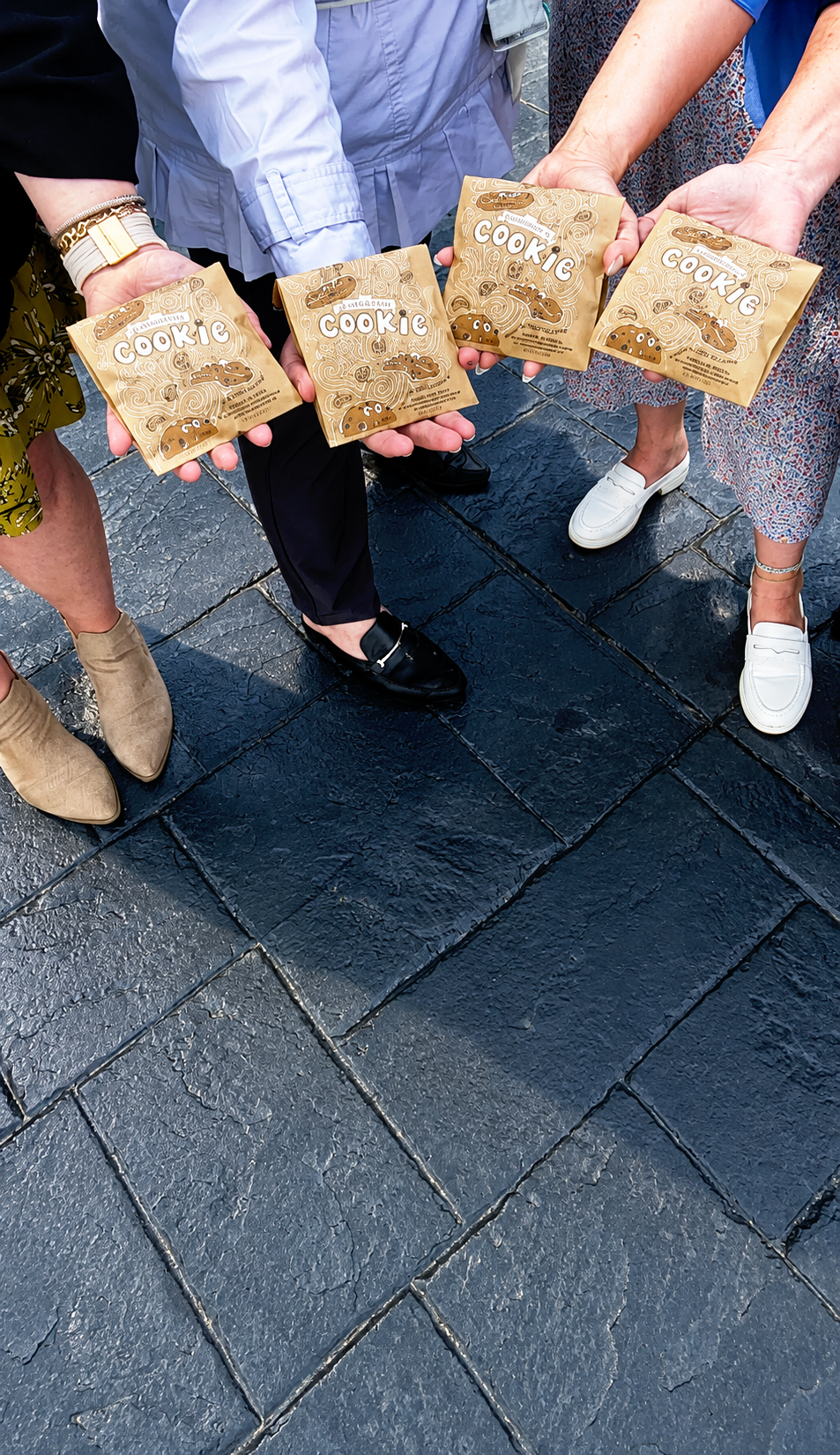 Four people standing on a cobblestone street, holding packages of the classic DoubleTree cookie.