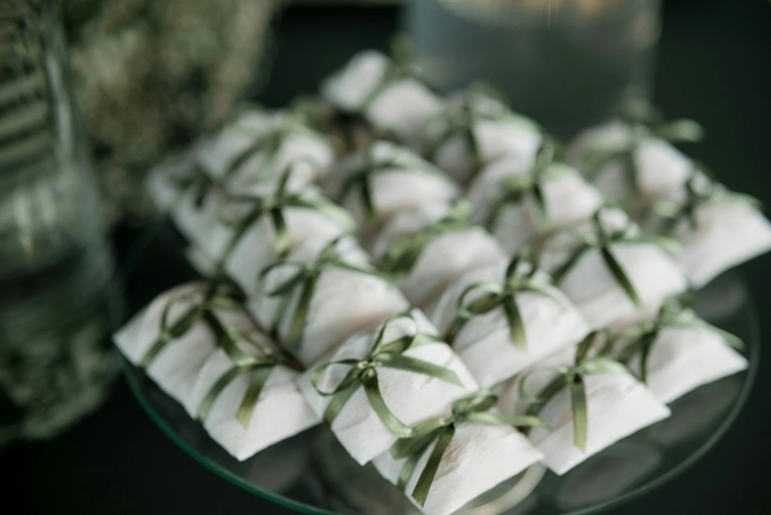 White favor boxes piled nicely on a table tied with green satin ribbon.