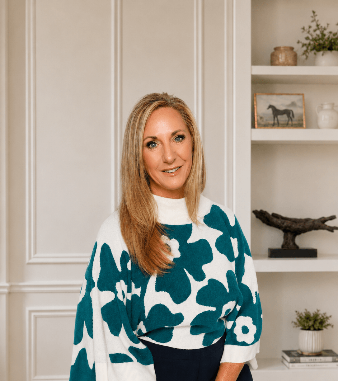 CoHost Works founder standing in a styled home interior with built-in shelving, warm decor, and a welcoming hospitality-focused feel.