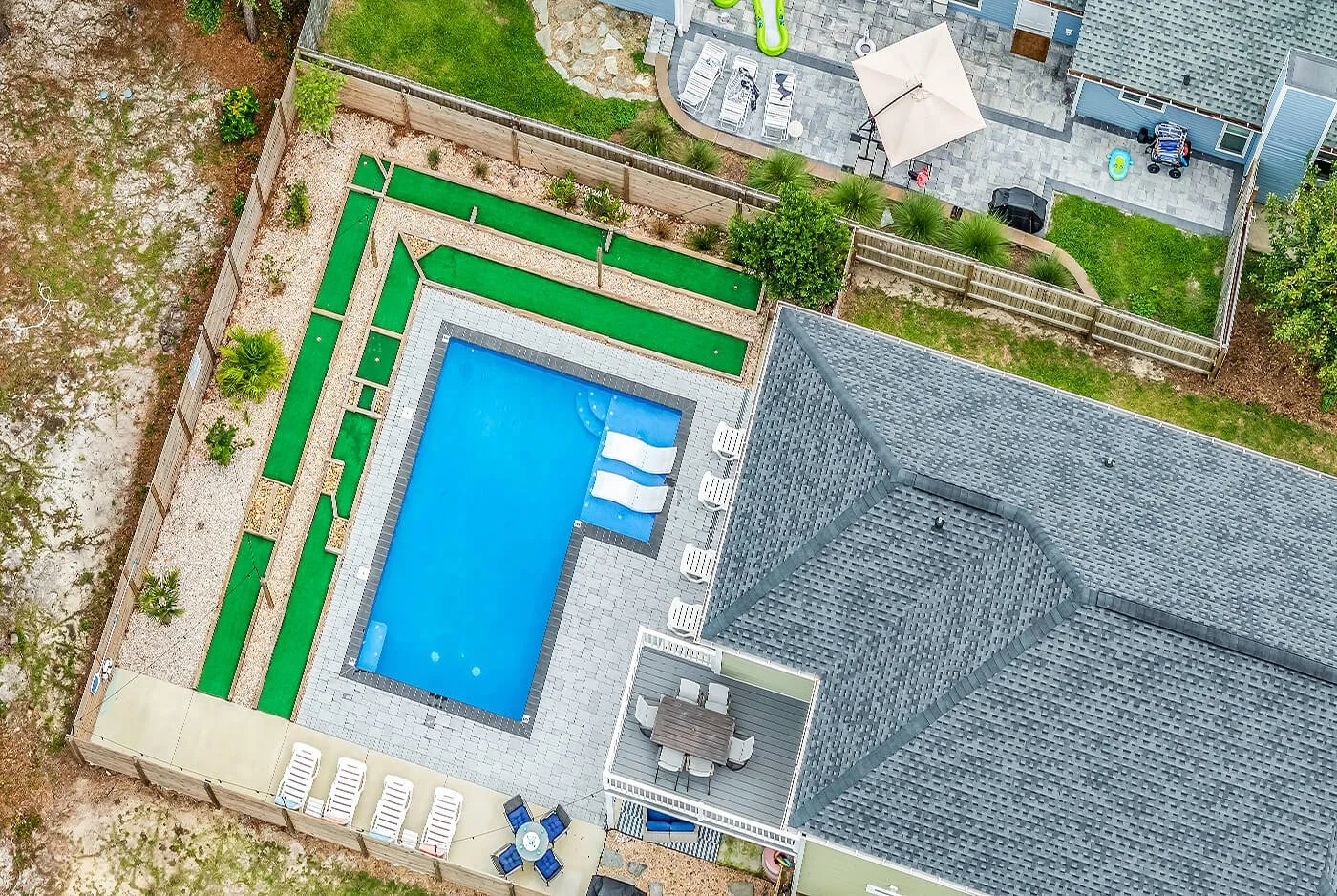 Aerial view of a CoHost Works vacation rental backyard with a private swimming pool, patio seating, fenced lawn, and landscaped outdoor space.