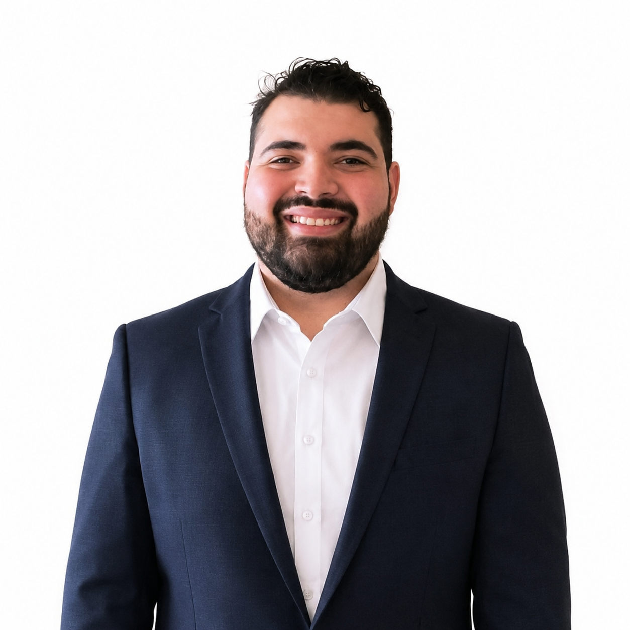 A man with dark hair and a beard smiling in a business suit and white shirt against a white background.