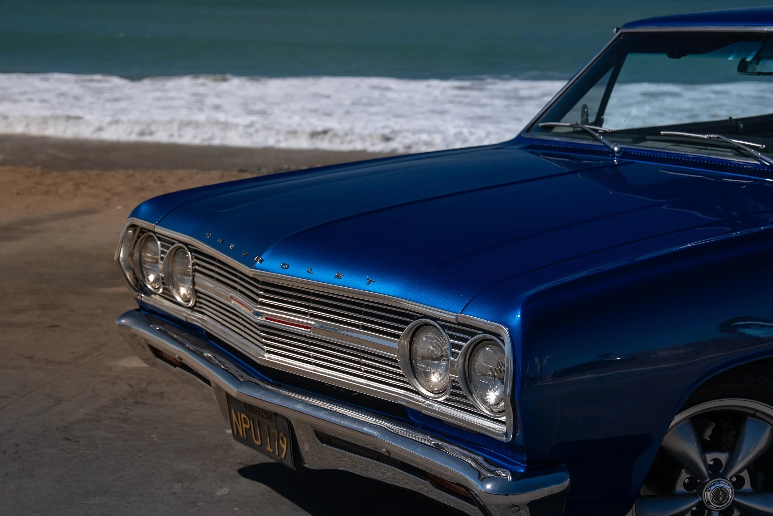 Close-up of a vintage Chevrolet car parked near the beach with ocean waves in the background.