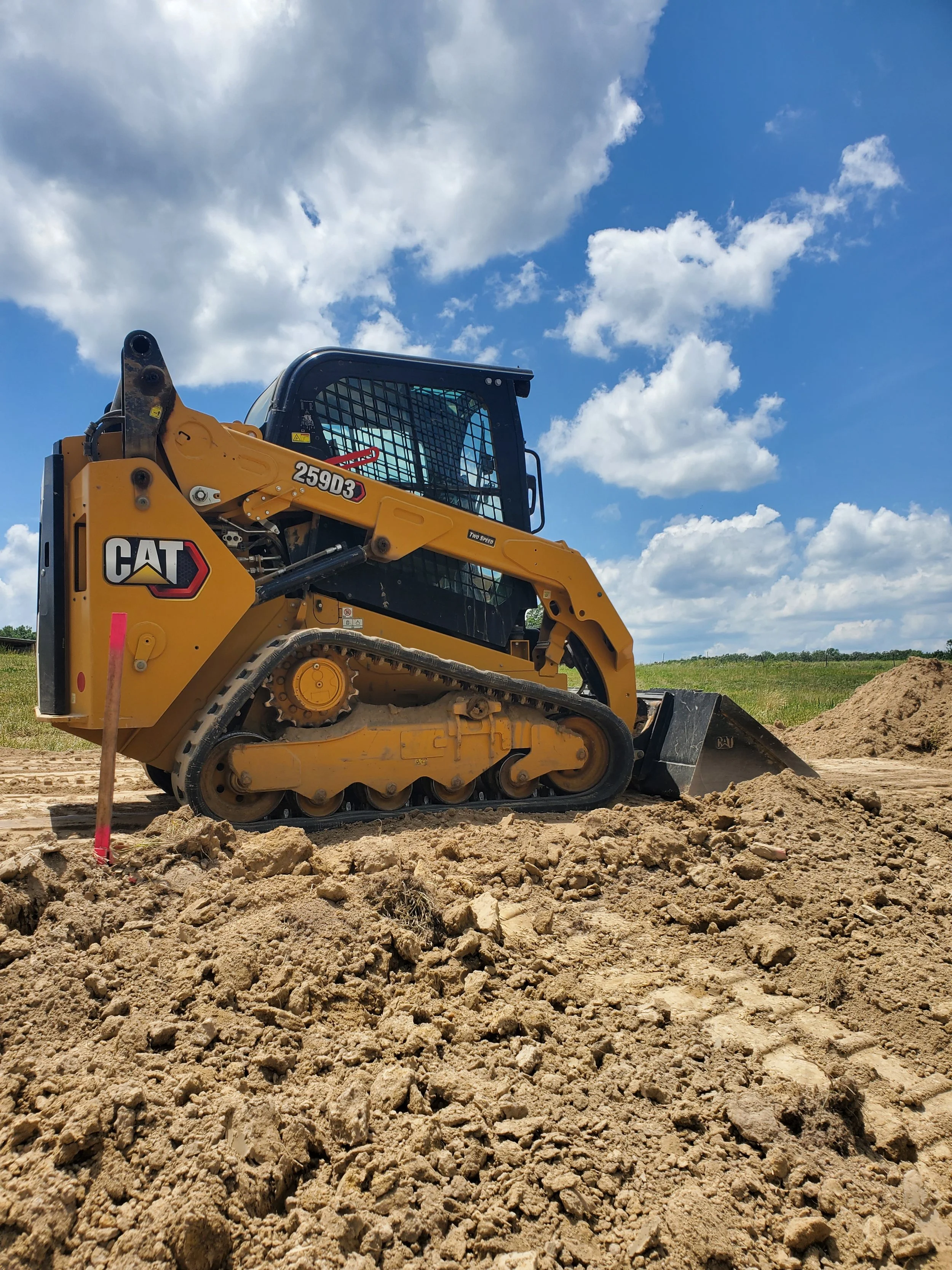 A yellow Caterpillar bulldozer working on a dirt construction site under a partly cloudy blue sky.