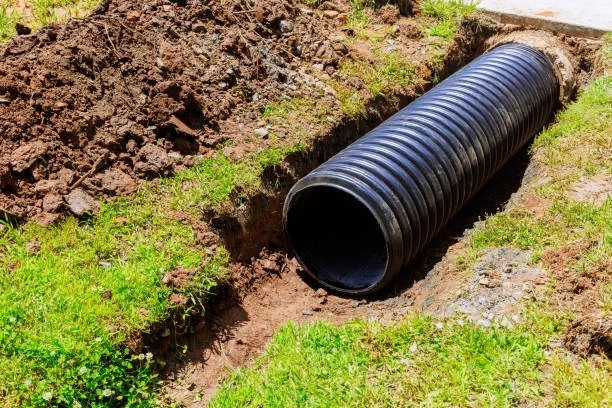 Black corrugated drainage pipe in a trench on a grassy area during installation.