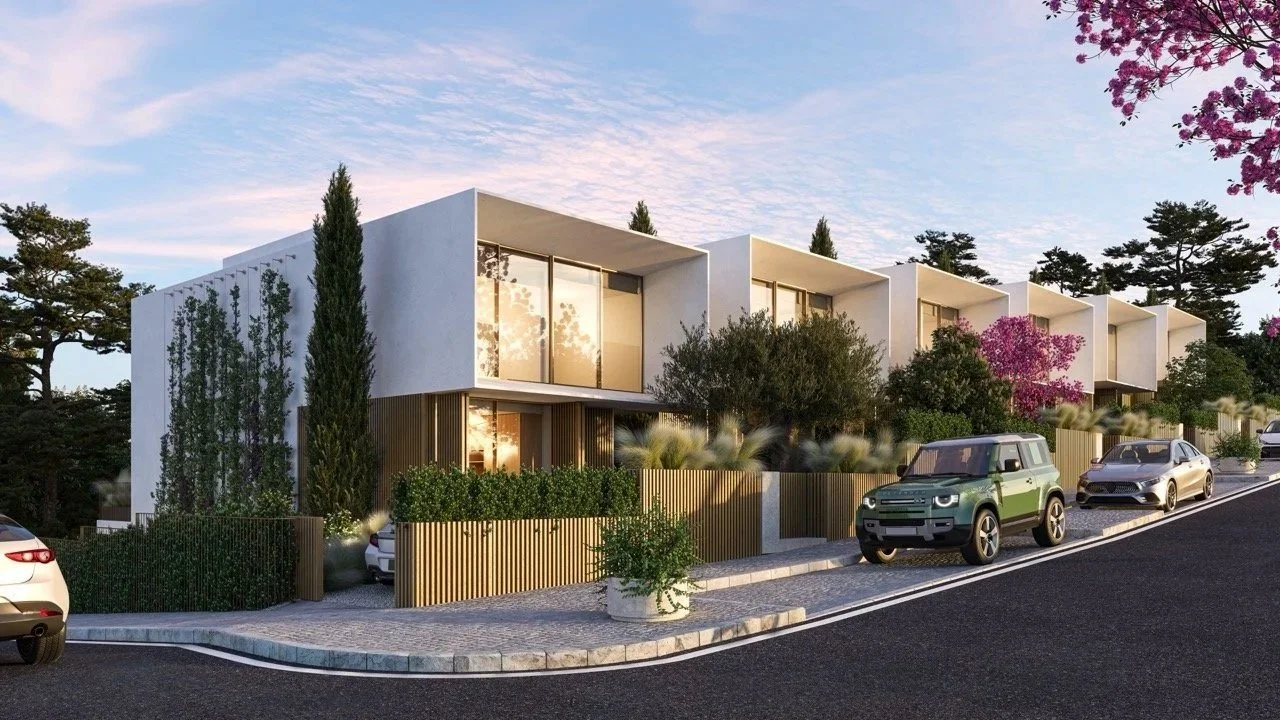 Modern multi-story residential building with large glass windows, surrounded by greenery, trees, and flowers, on a sloped street with parked cars.