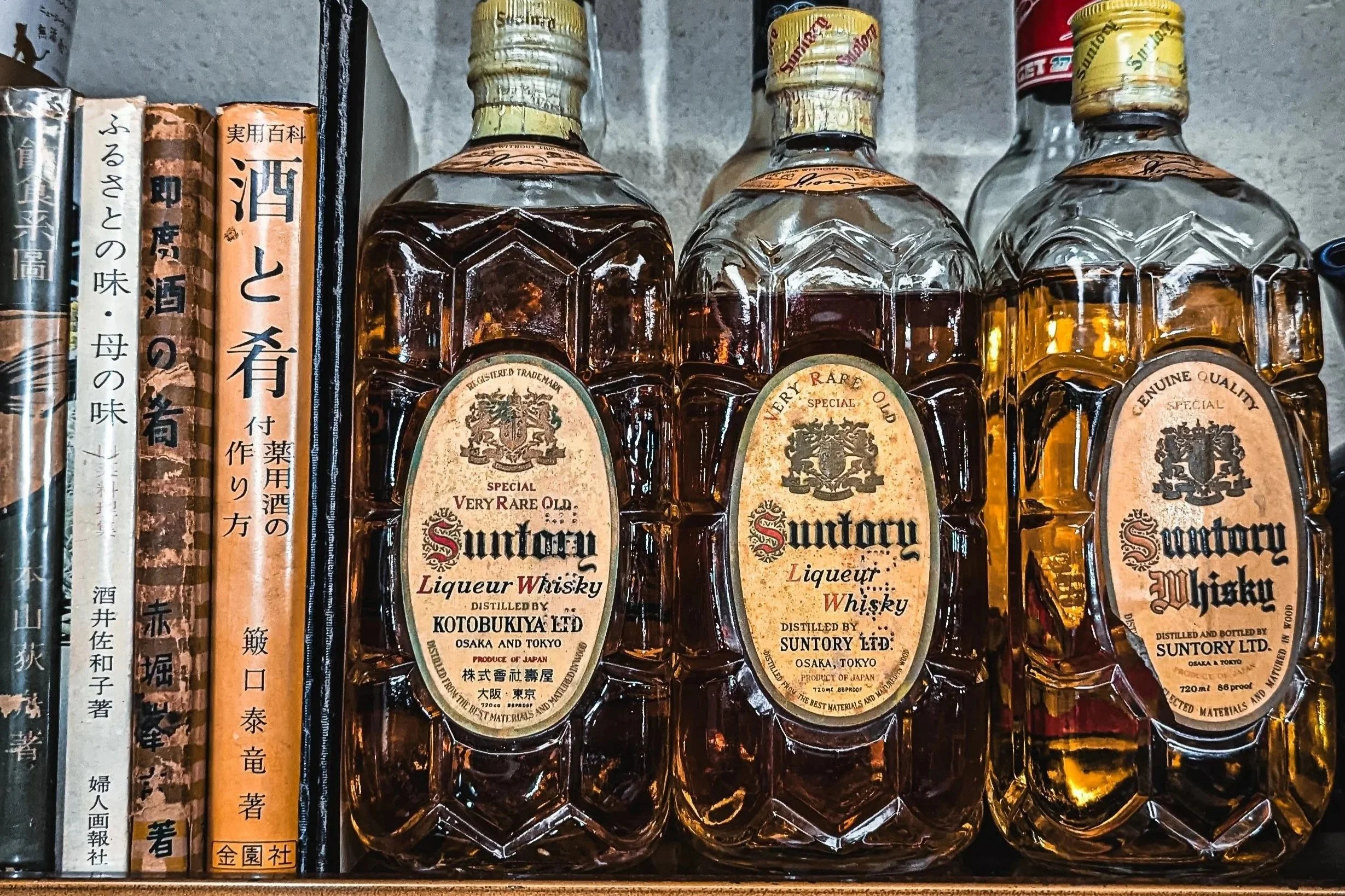 Row of Suntory whisky bottles on a shelf with Japanese books on the side.