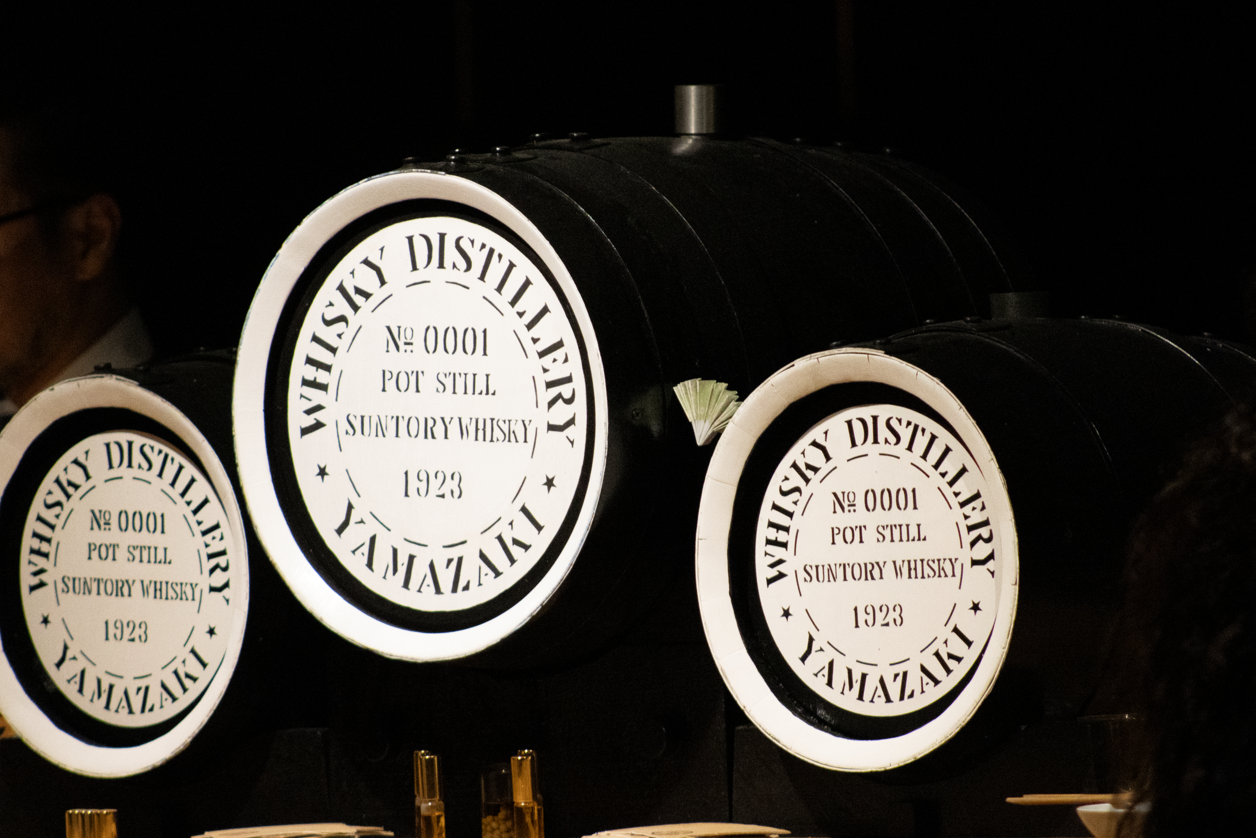Multiple whiskey barrel labels displaying 'Wahay Distillery No 0001 Pot Still Suntory Whisky 1923,' stacked in a dark setting.