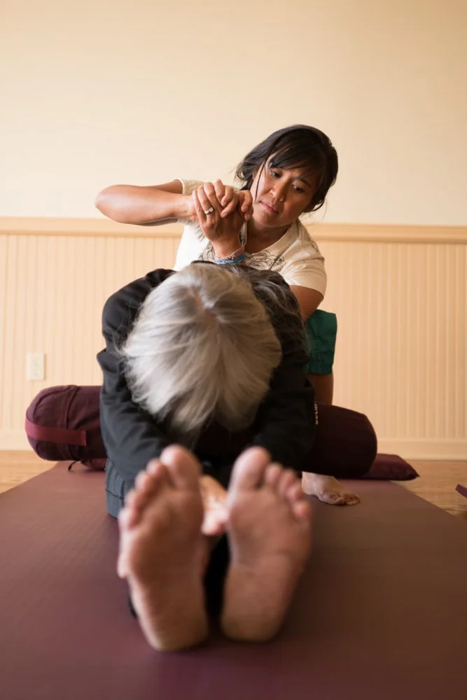 Thai massage practitioner applying pressure to a patient's back while the patient is reaching for her toes