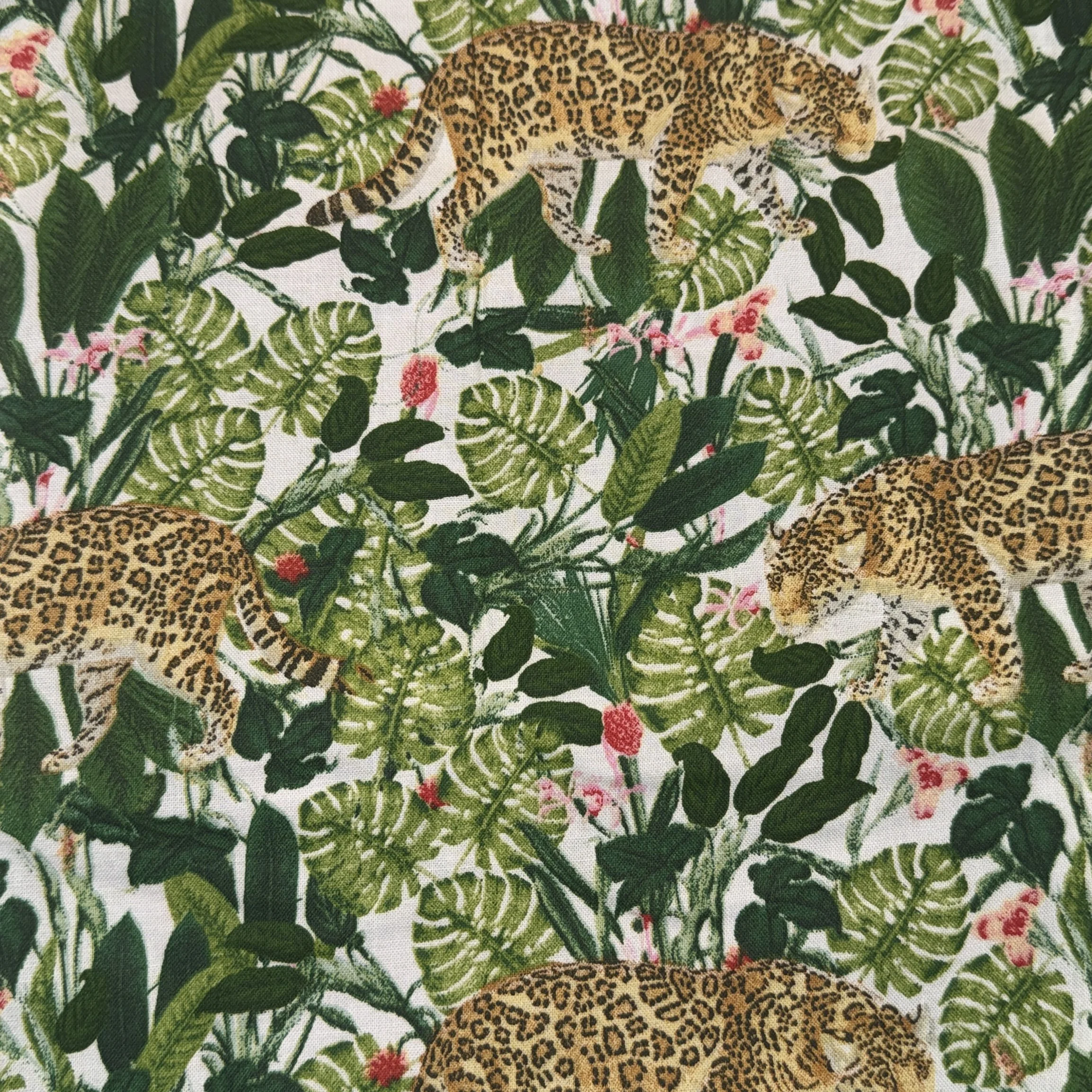 Fabric pattern featuring leopards walking among tropical green leaves and pink flowers.