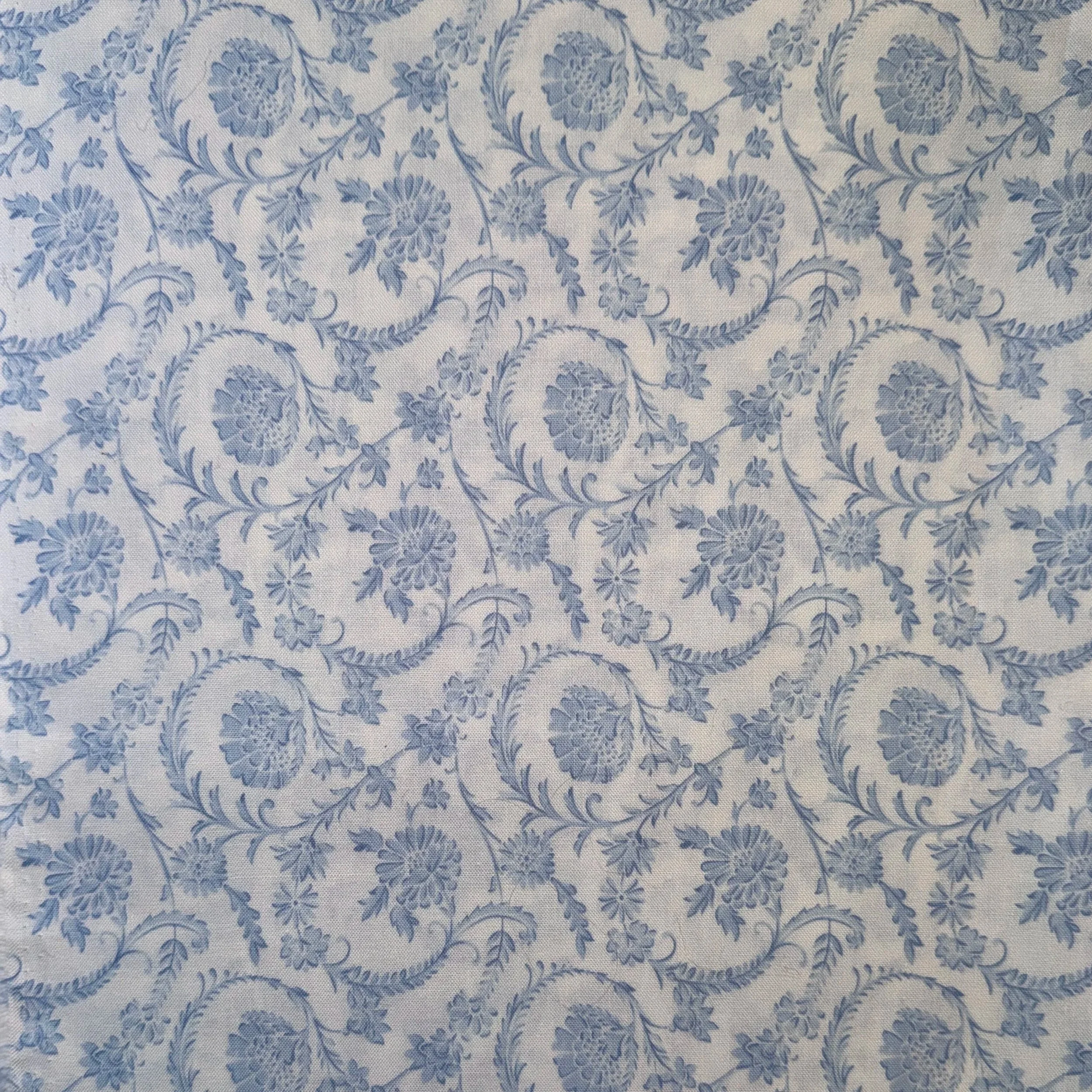 Close-up of a fabric with a light-colored background and a detailed blue floral pattern of swirling vines, flowers, and leaves.