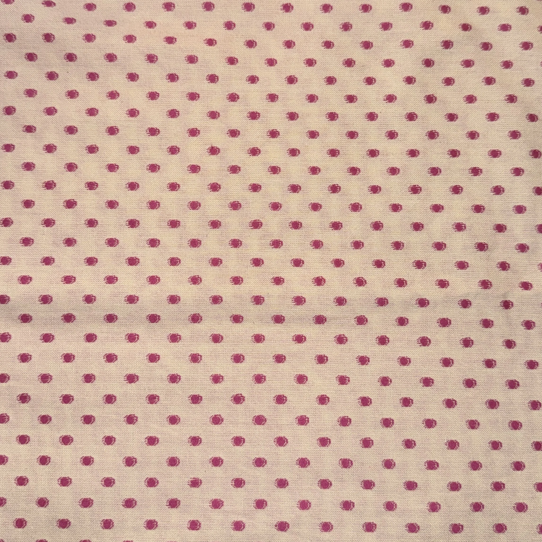 Close-up of fabric with a pattern of small pink polka dots on a cream background.