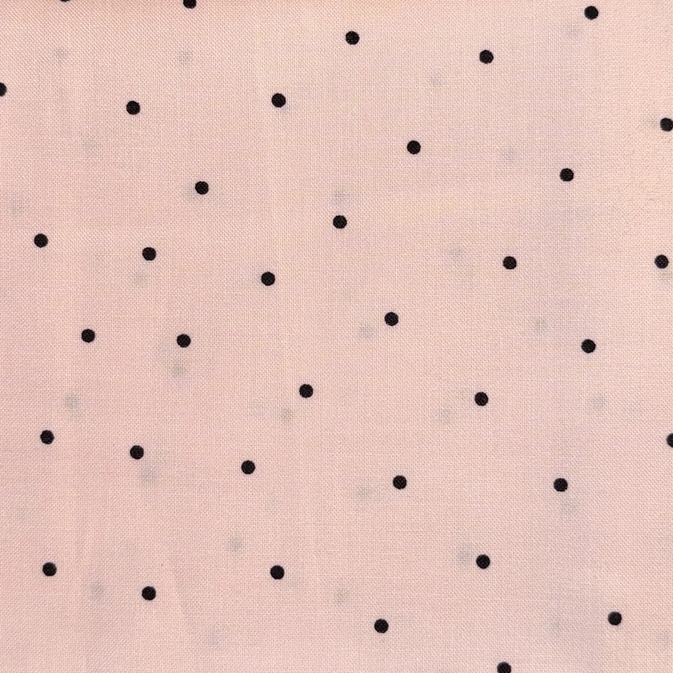 Close-up image of a pink fabric with irregularly spaced small black polka dots.