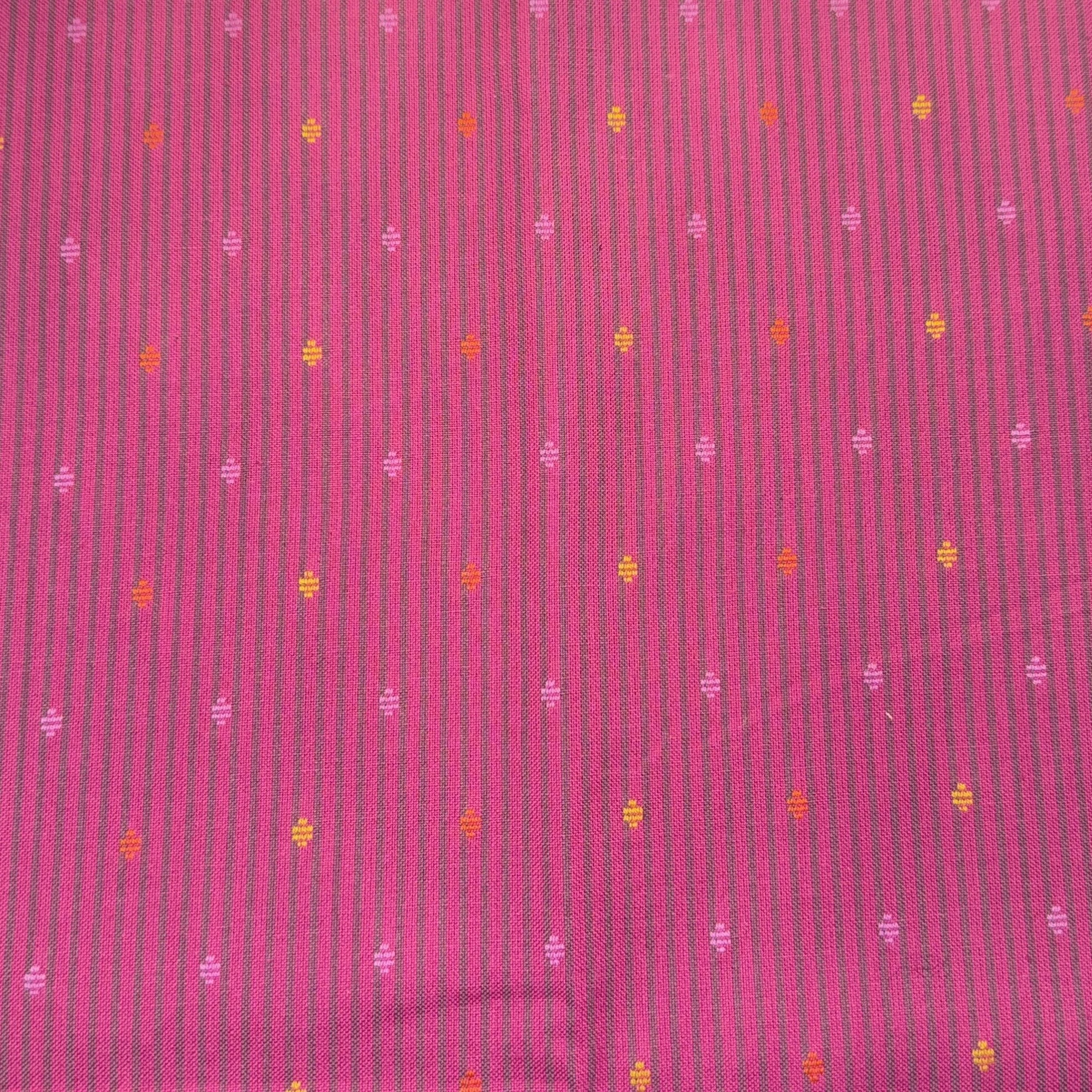 Close-up of a pink fabric with small embroidered yellow, orange, and purple floral patterns arranged in rows.