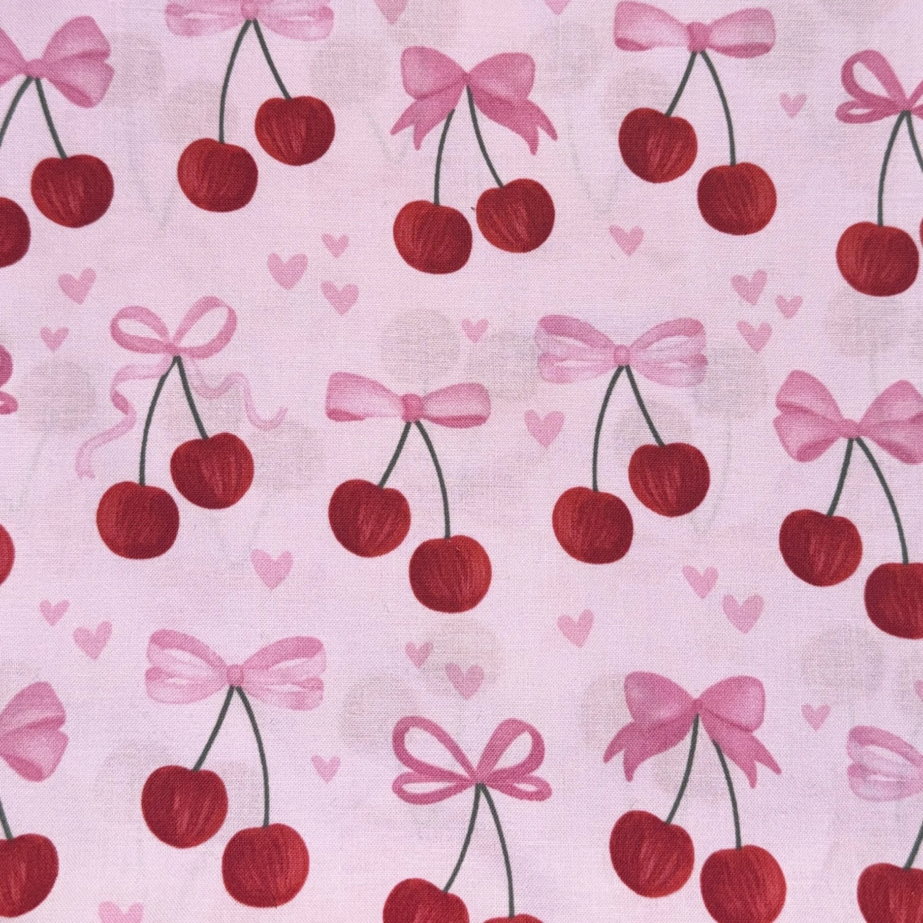 Pink fabric with a pattern of red cherries tied with pink bows and small pink hearts.