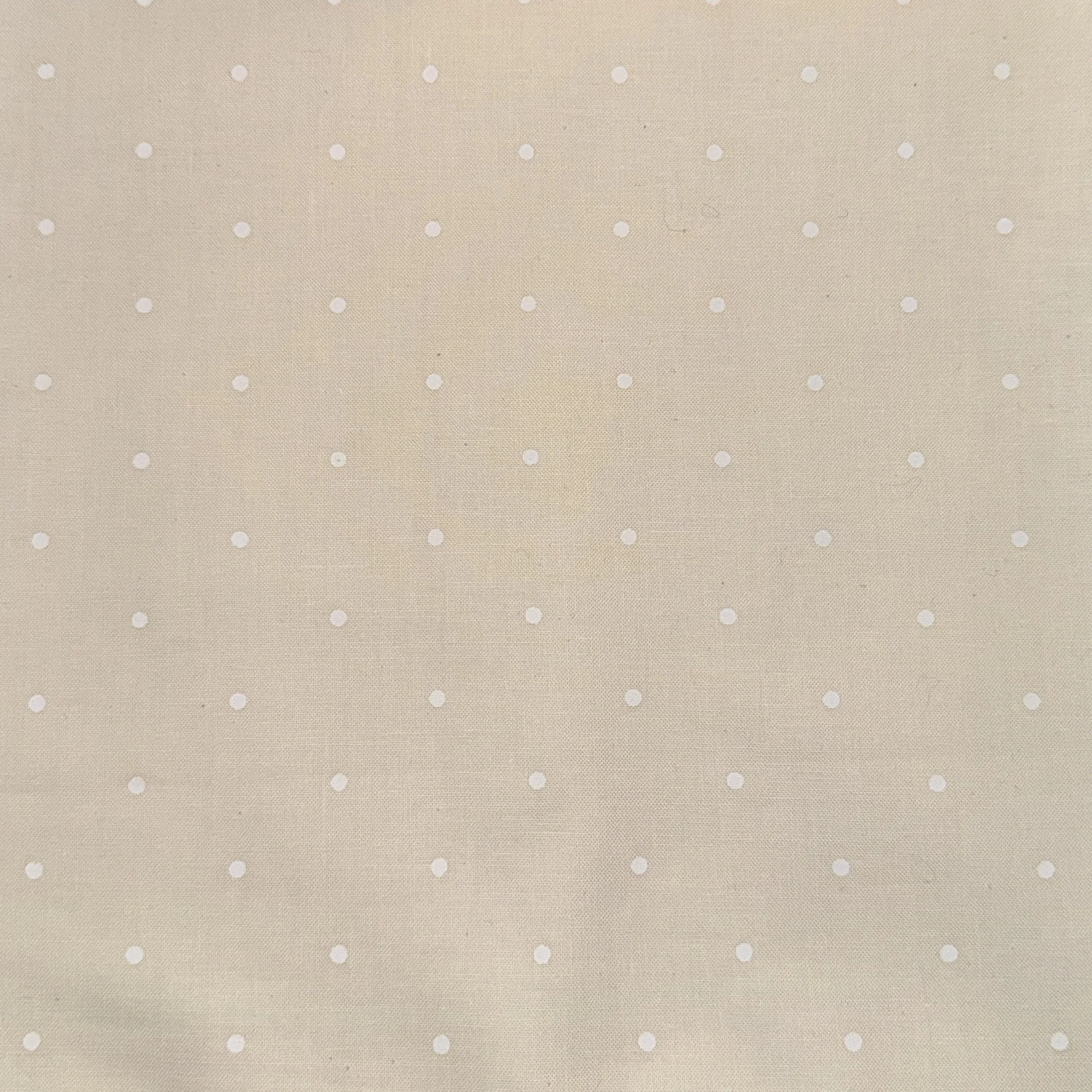 A beige fabric background with small white polka dots evenly spaced.