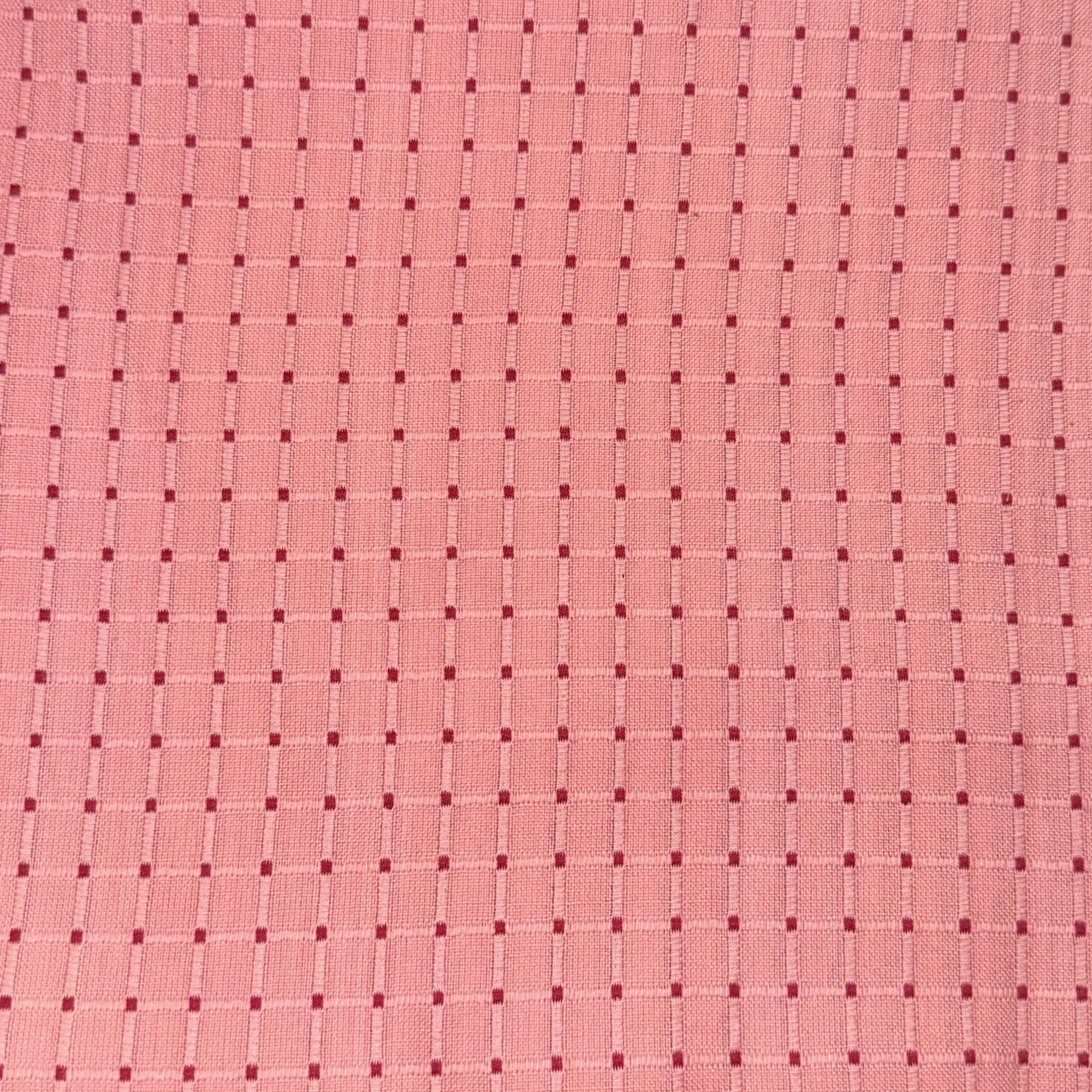 Close-up of pink fabric with a grid pattern of small red squares.