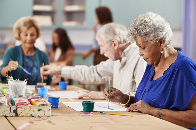 Older adults participating in a painting class at a table with paint supplies.