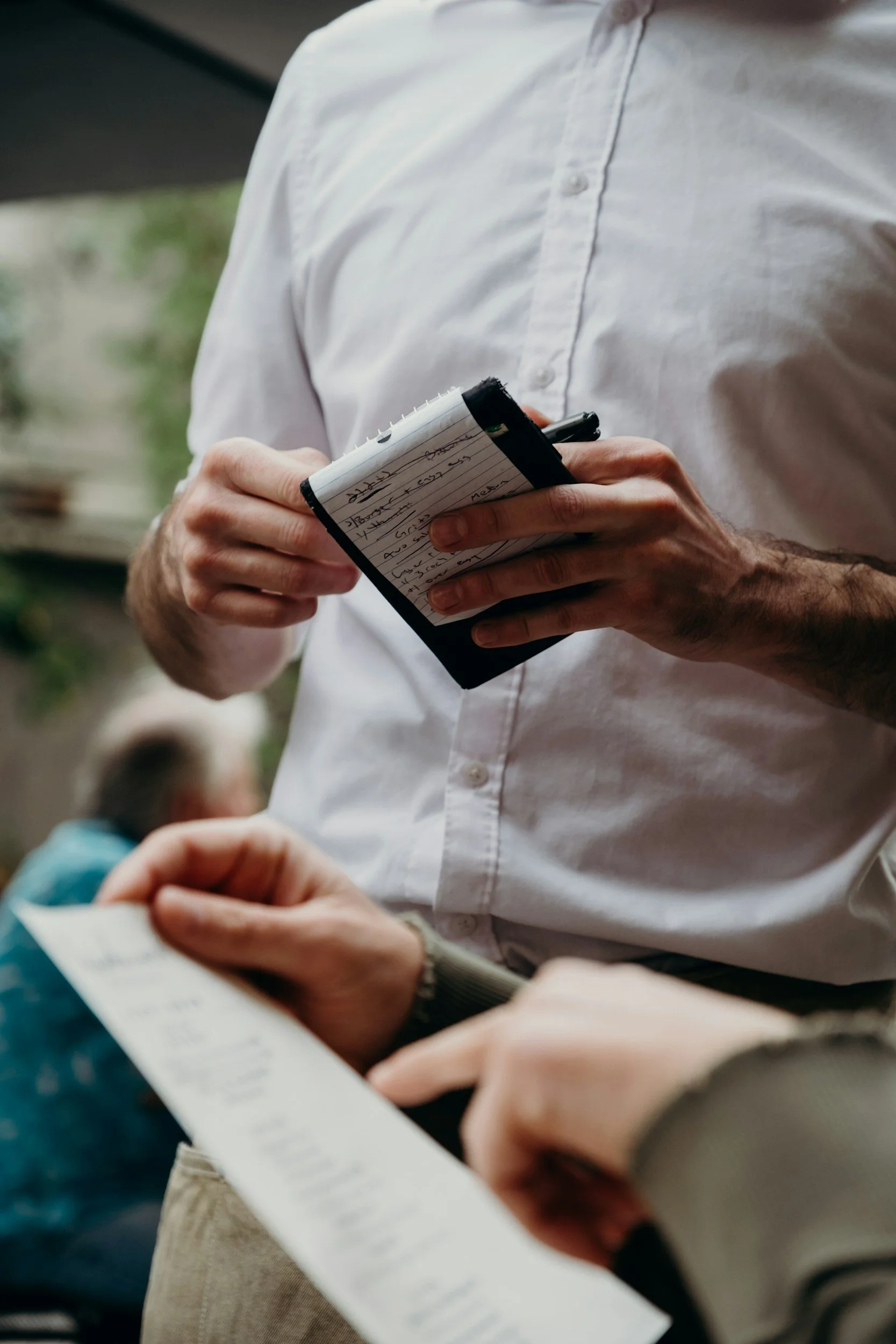Person wearing a white shirt holding a notepad with handwritten notes.