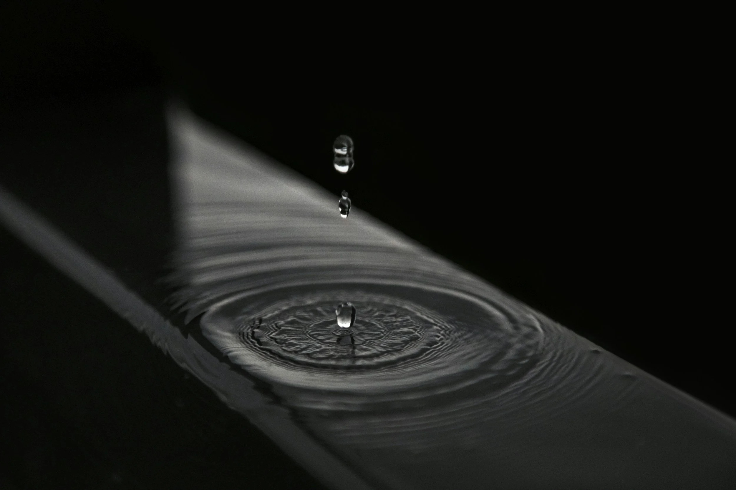 Close-up of a water droplet falling into a pool, creating ripples with a dark background.