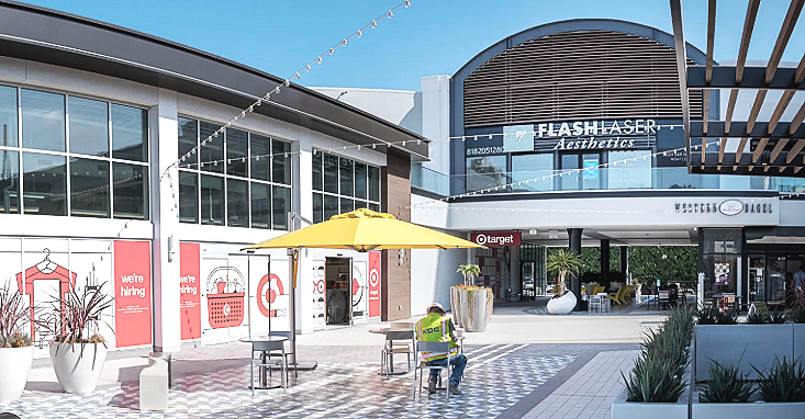 An outdoor shopping mall area with a Target store, a yellow umbrella, and a person in a reflective vest cleaning the ground.