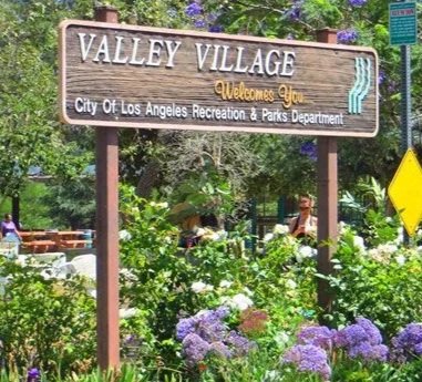Welcome sign for Valley Village, a neighborhood in Los Angeles, California, with flowers and trees in the background.