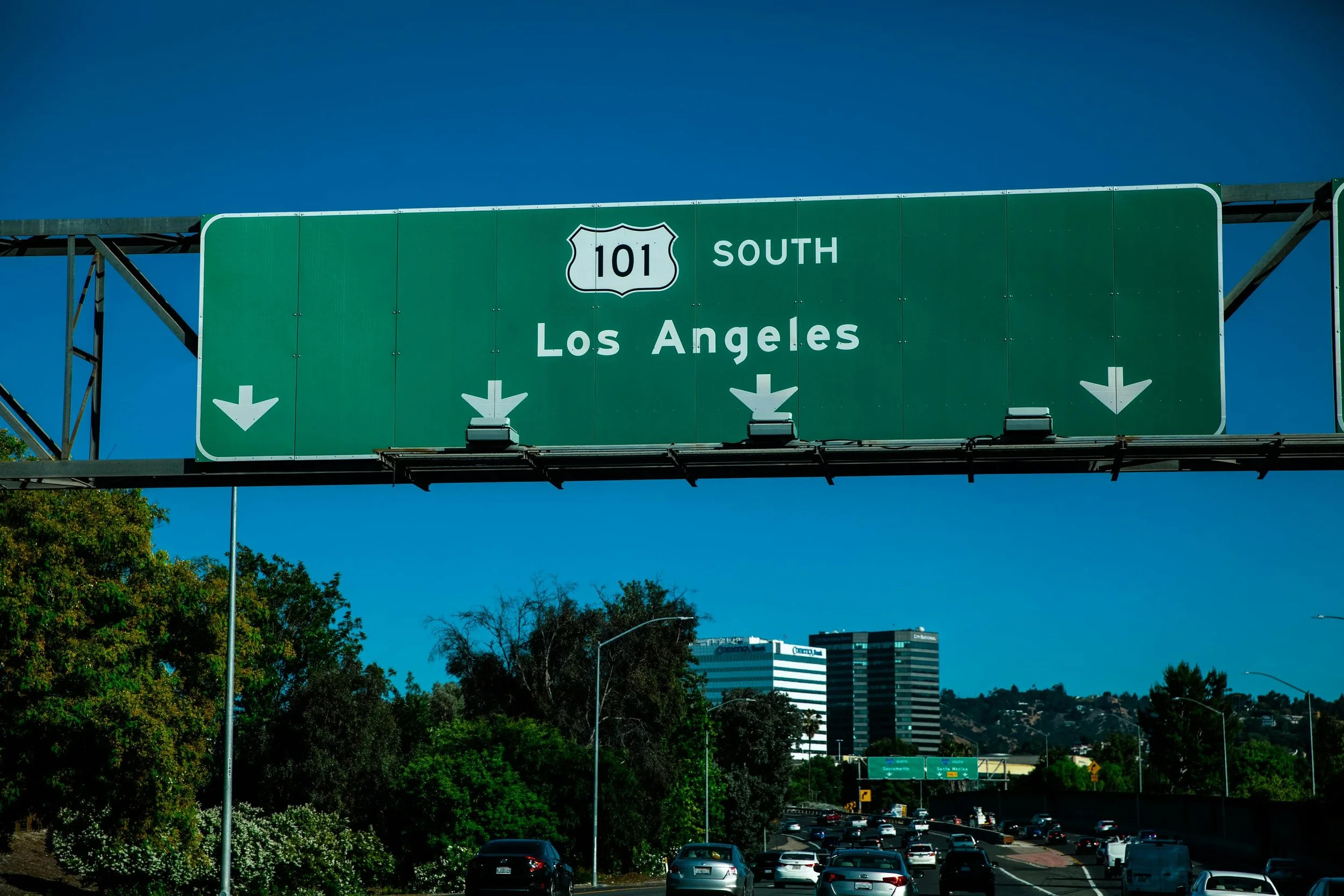 Highway sign indicating southbound route 101 to Los Angeles with traffic below and city buildings in the background.
