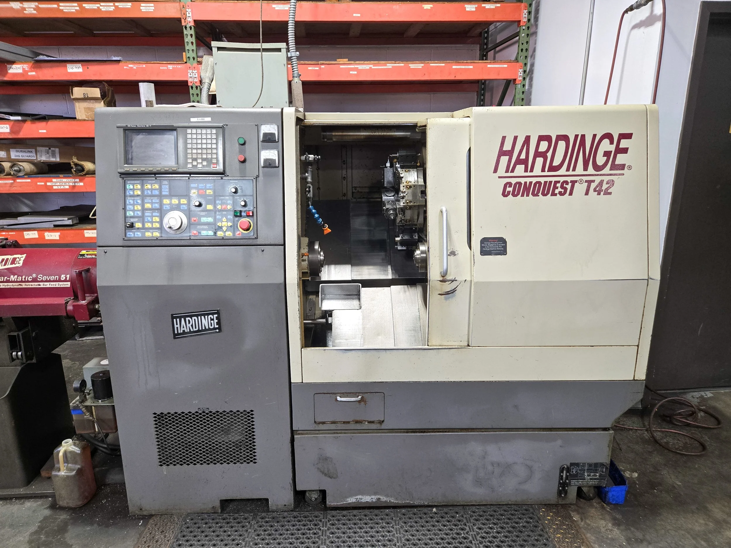Industrial CNC machine labeled 'HARDINGE CONQUEST T42' in a workshop setting with storage shelves behind it.