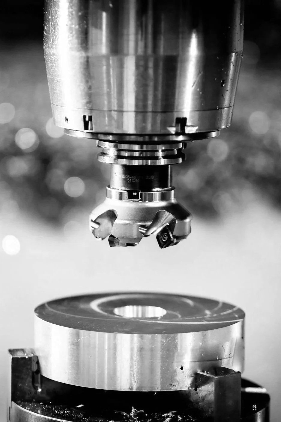 Close-up of a CNC machine tool and workpiece in a manufacturing setting, in black and white.