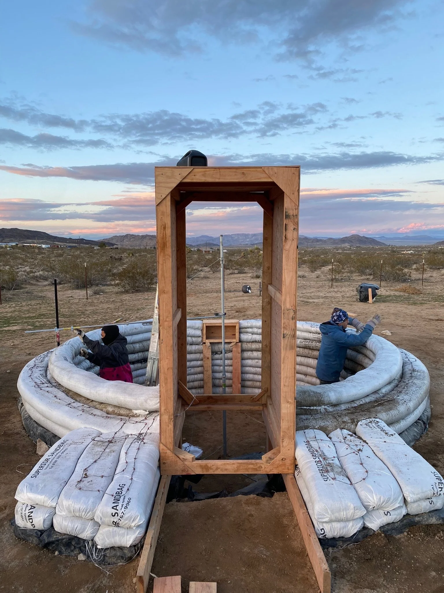 Construction workers installing a wooden frame in a geothermal plant with a desert landscape and mountains in the background during sunset.