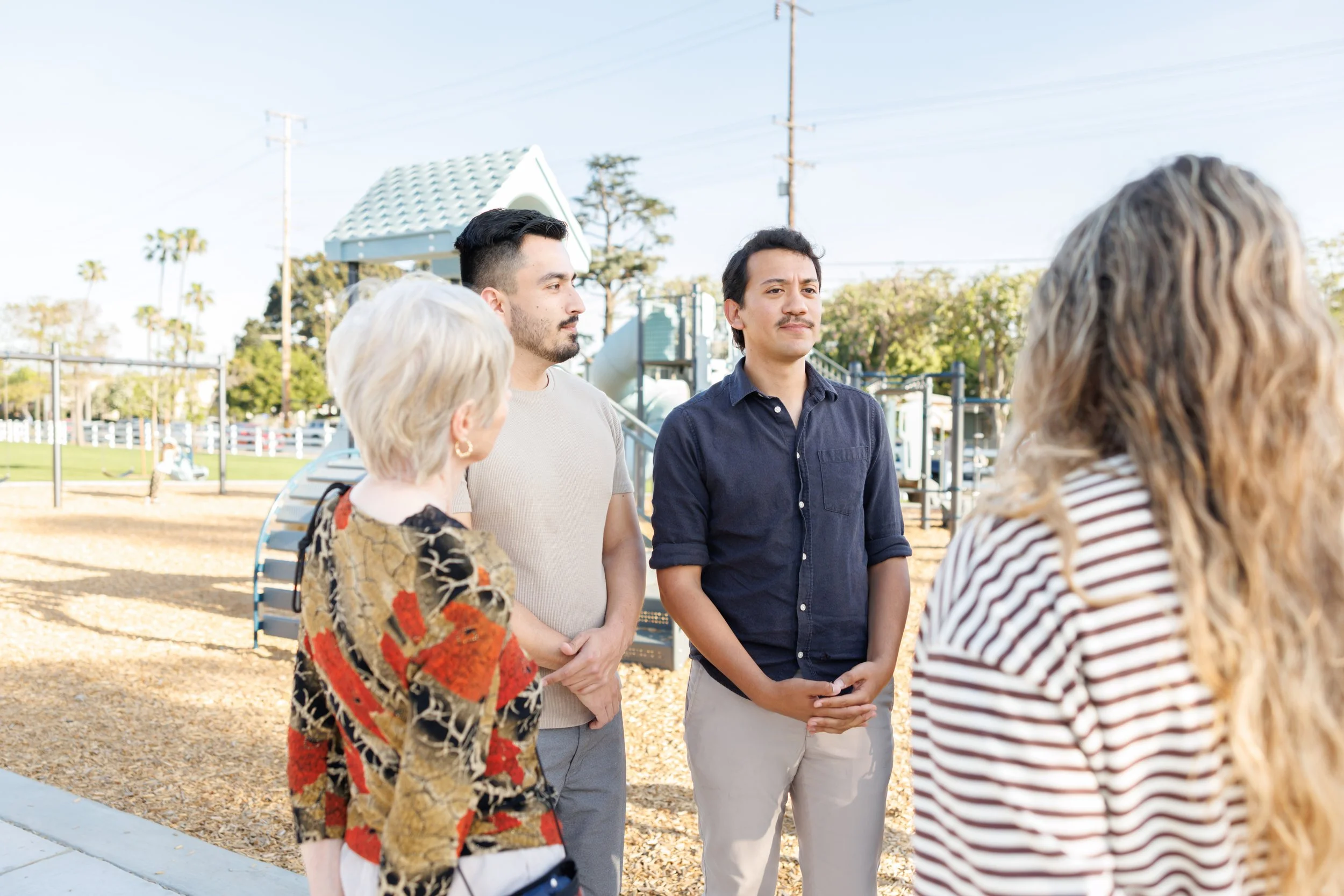 A group of five diverse adults talking outdoors in a park-like setting during the daytime.